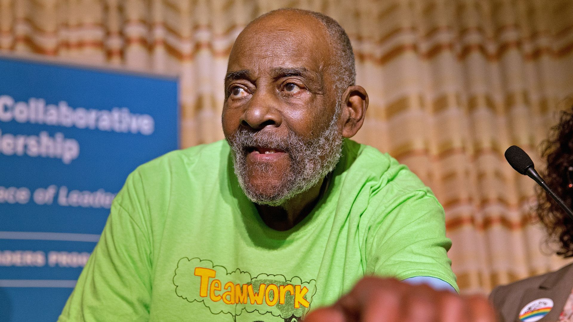 Mel King is pictured at the Building a Better Boston breakfast, where he got an award. He's wearing a green T-shirt that says "Teamwork makes the dream work."