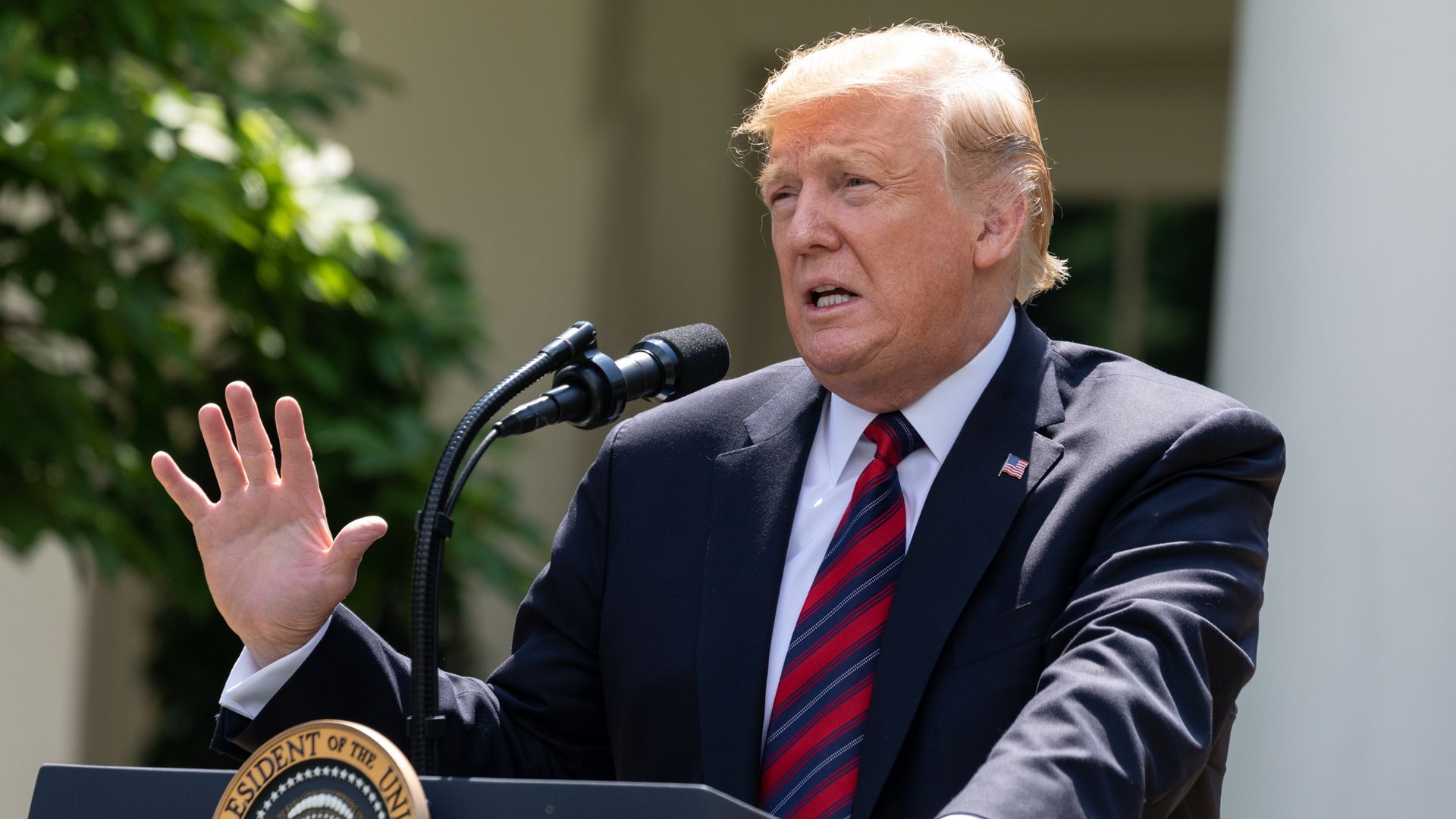 In this image, Trump stands and speaks into a microphone on a podium.
