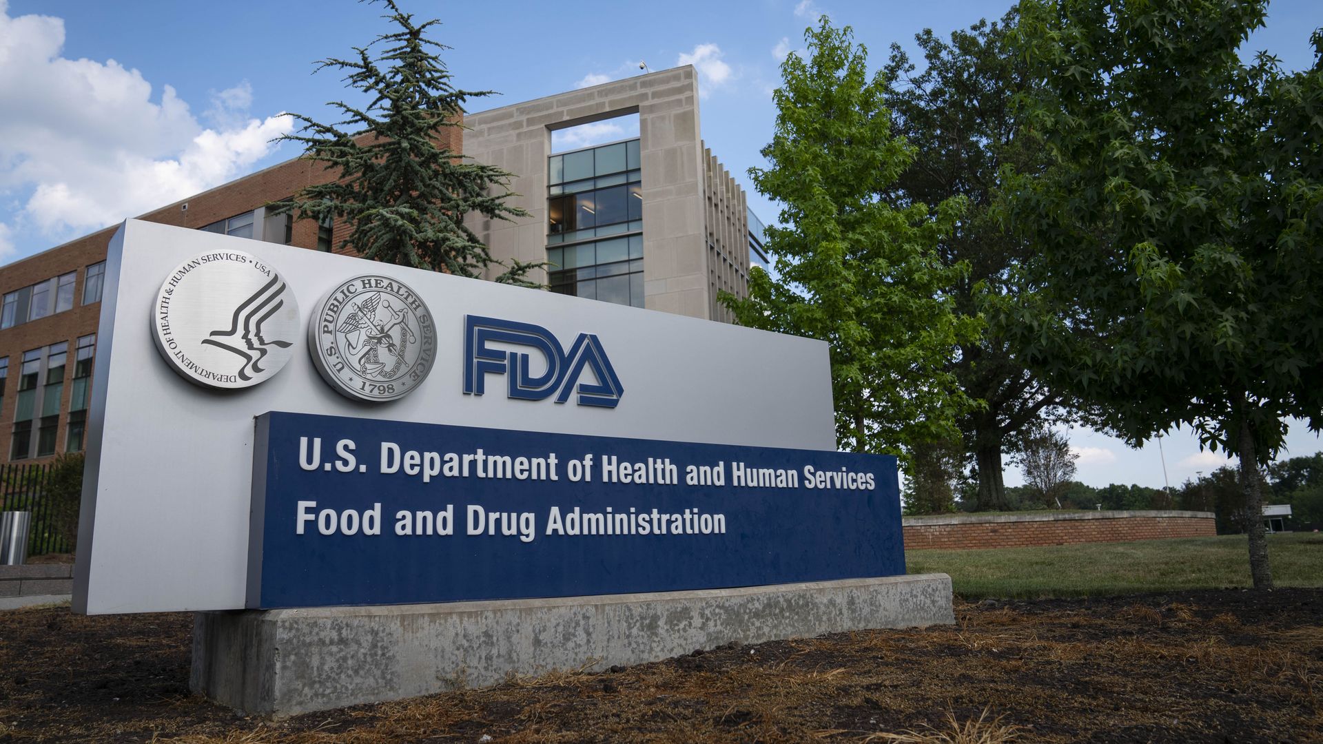 The FDA headquarters sign in front of trees and the FDA building.