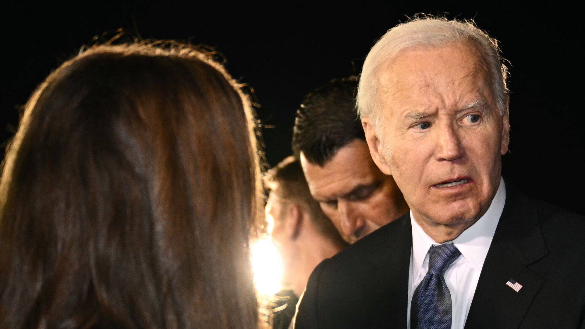 President Biden, wearing a black suit, speaking to a supporter in the dark while surrounded by his security detail.