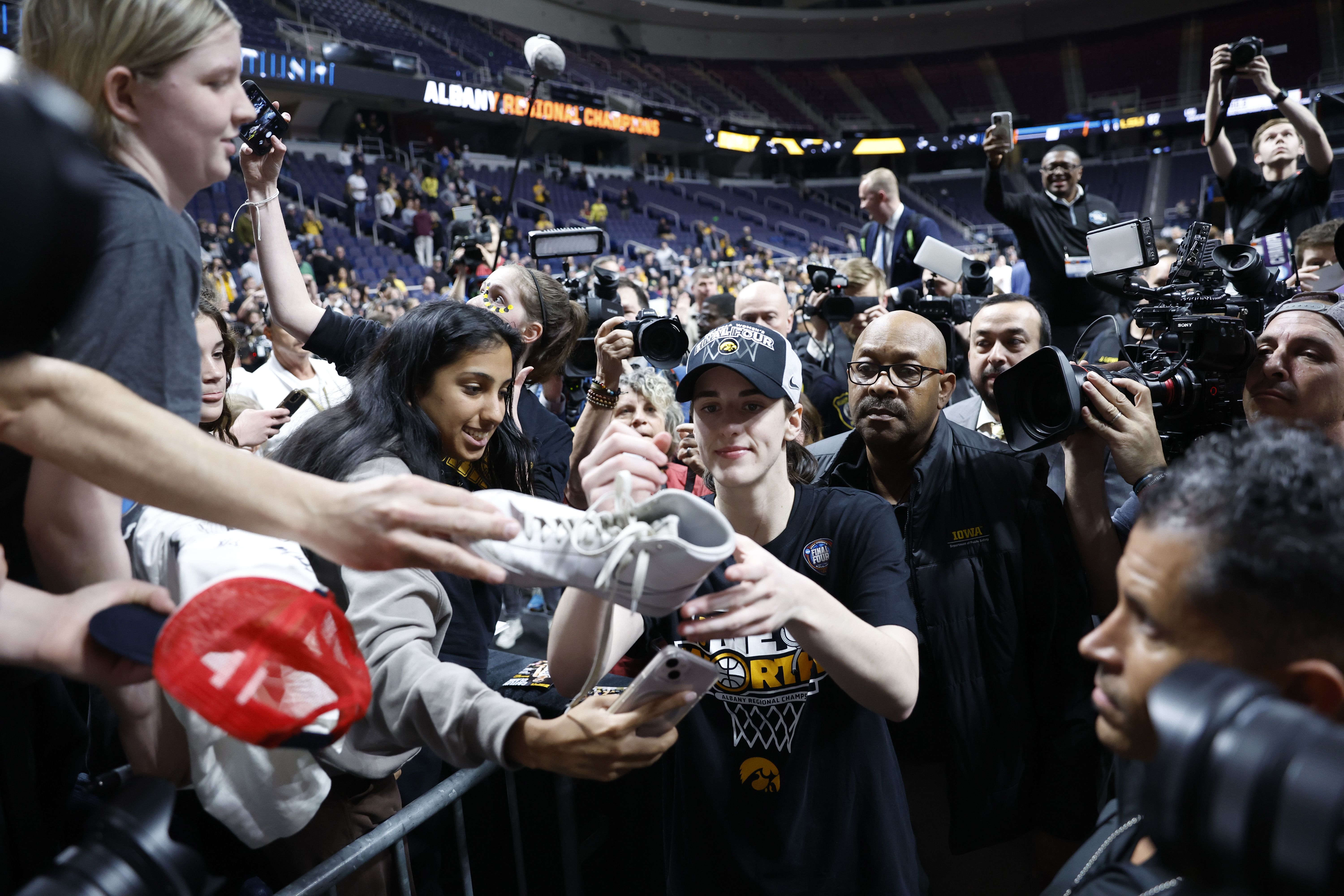 Caitlin Clark of Iowa signs a bunch of hats and autographs as she walks off the court wearing a black shirt