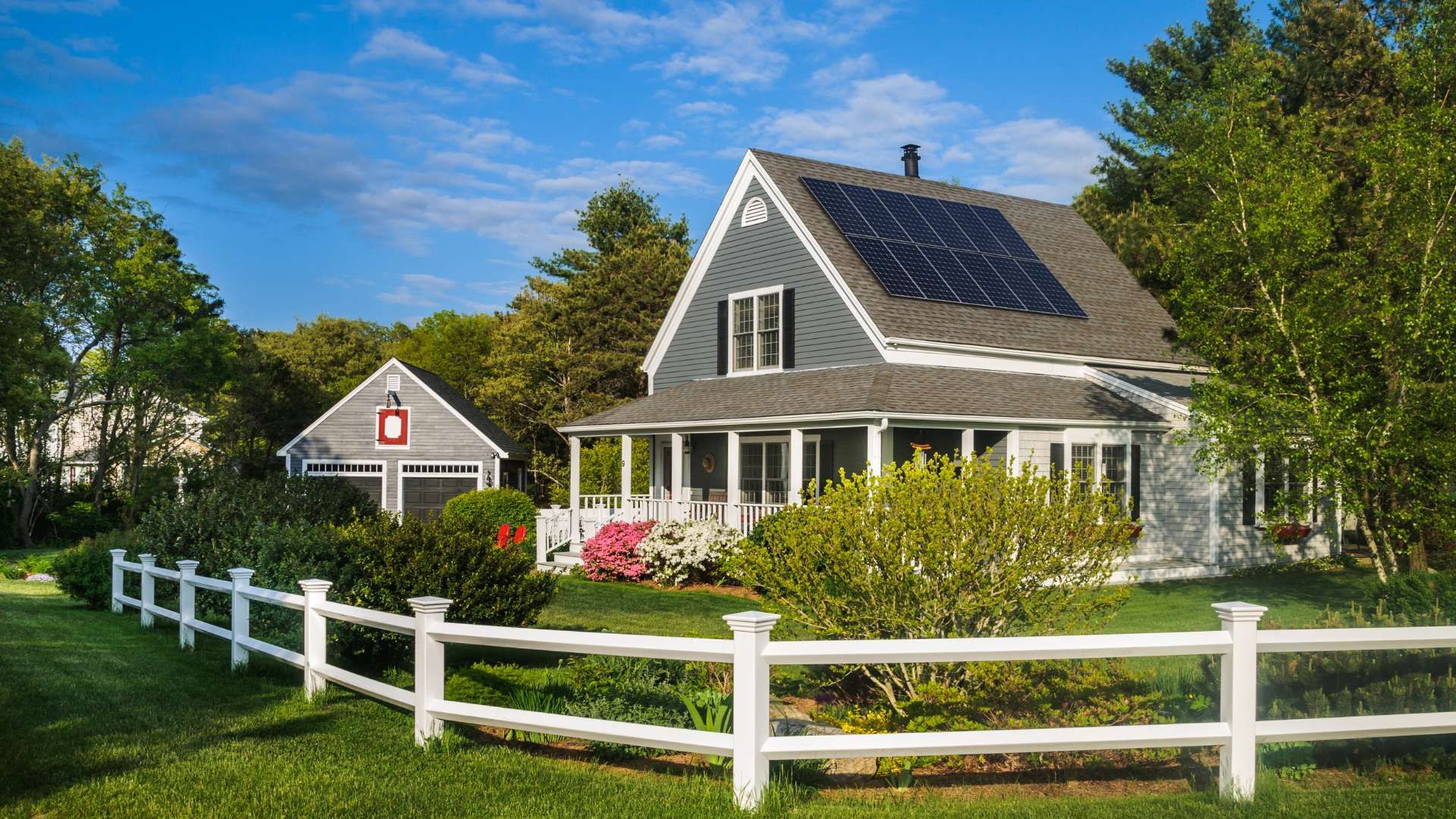 A house with a detached garage and a white fence. There are solar panels on the roof. 