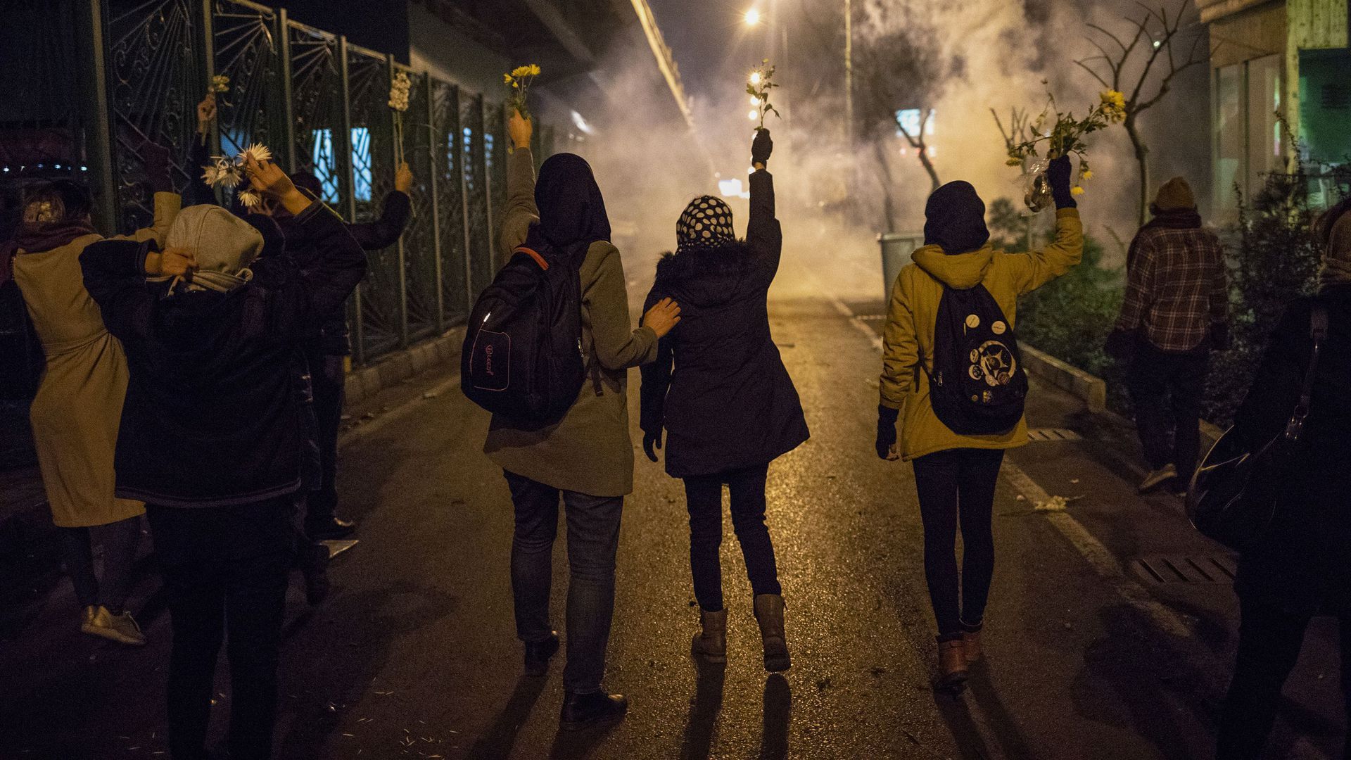 Iranian protesters hold flowers as riot police fire tear gas during a demonstration in front of Tehran's Amir Kabir University