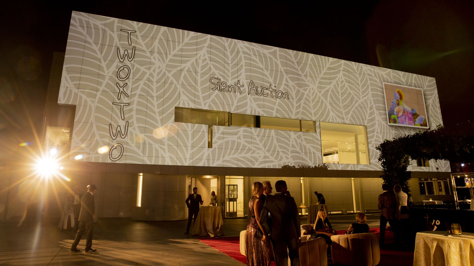 A boxy building with lights projected on its facade and "Silent Action" and "Two x Two" projected on it