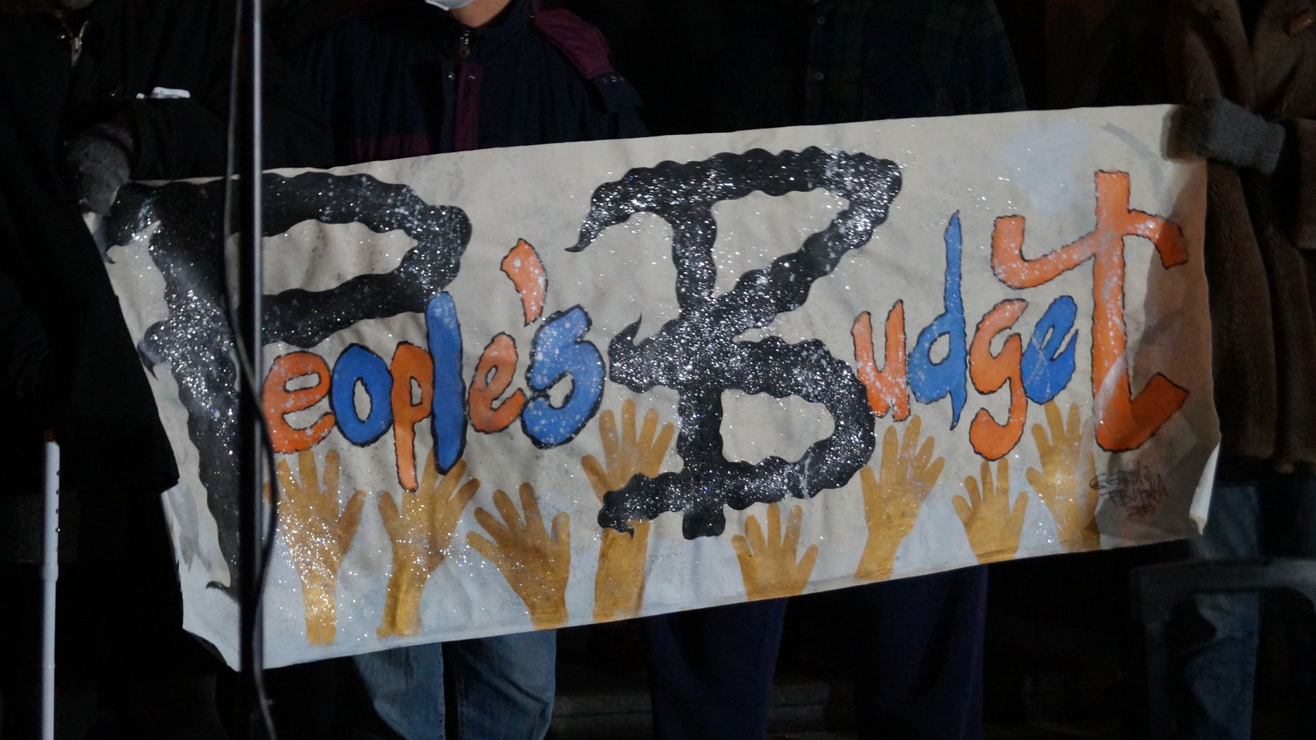 A handmade sign reading "People's Budget" held at night