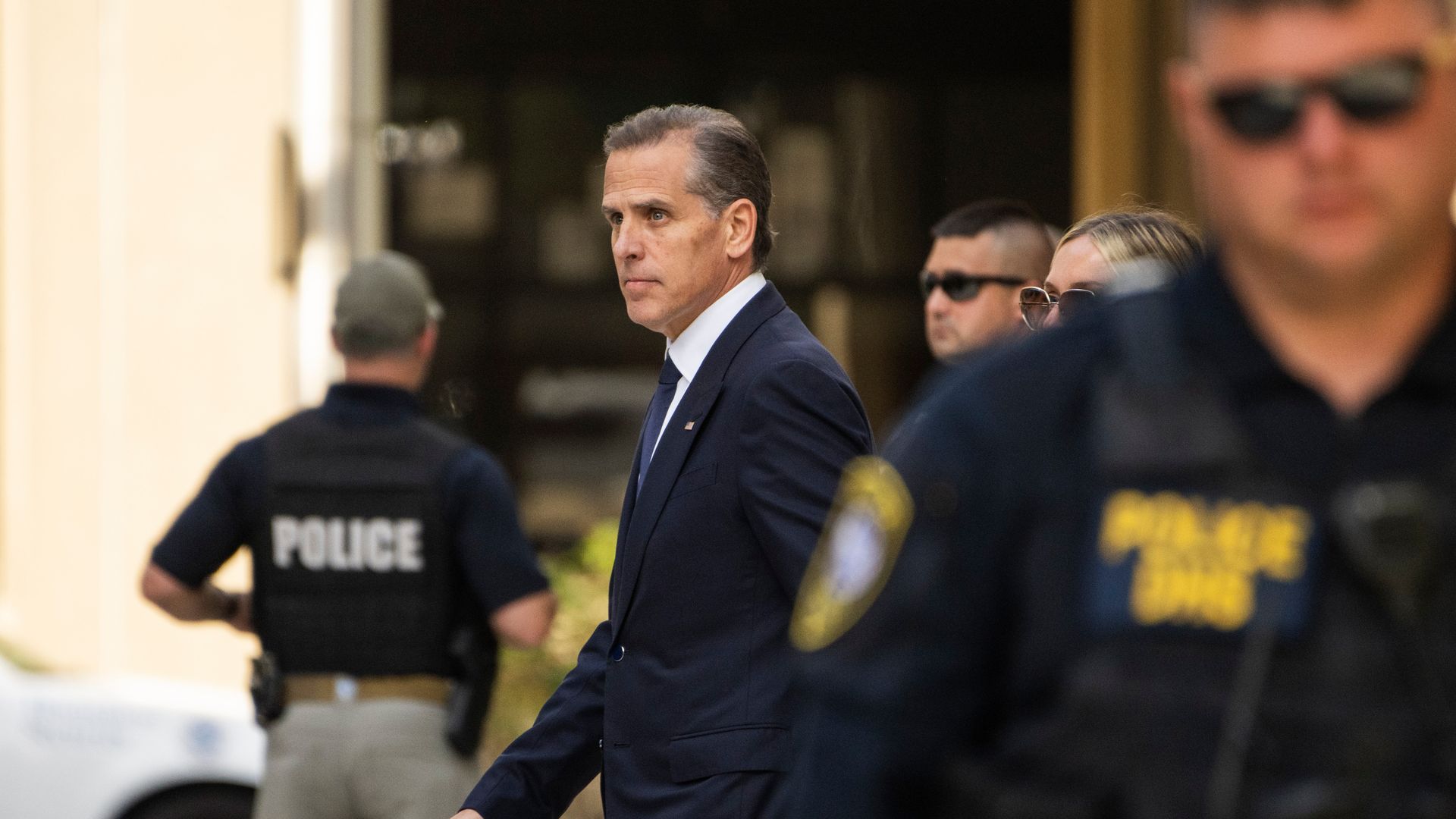 Hunter Biden, in a dark suit, walks to court between law enforcement officers.