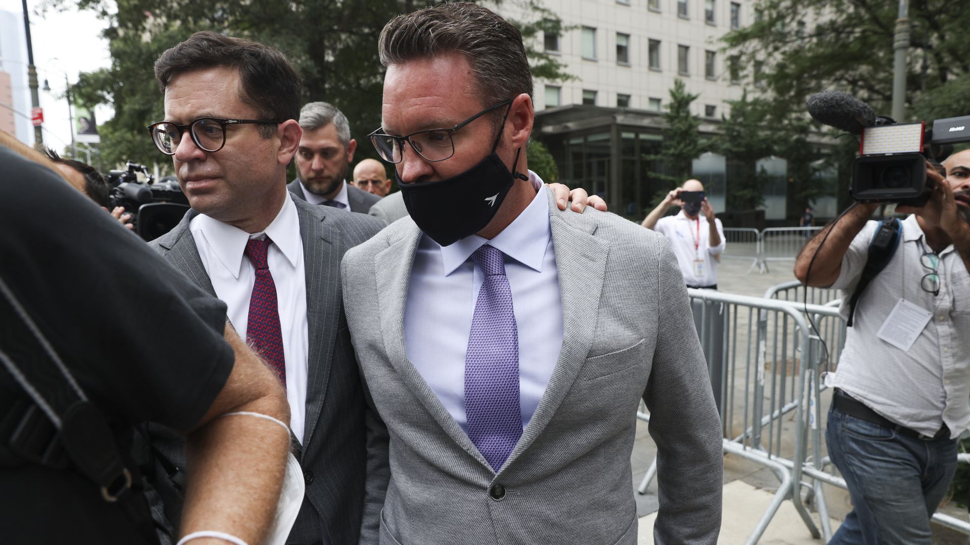 The former CEO of Nikola, Trevor Milton, wearing a gray suit, purple tie and white shirt, walks near a courthouse with a lawyer at his side.