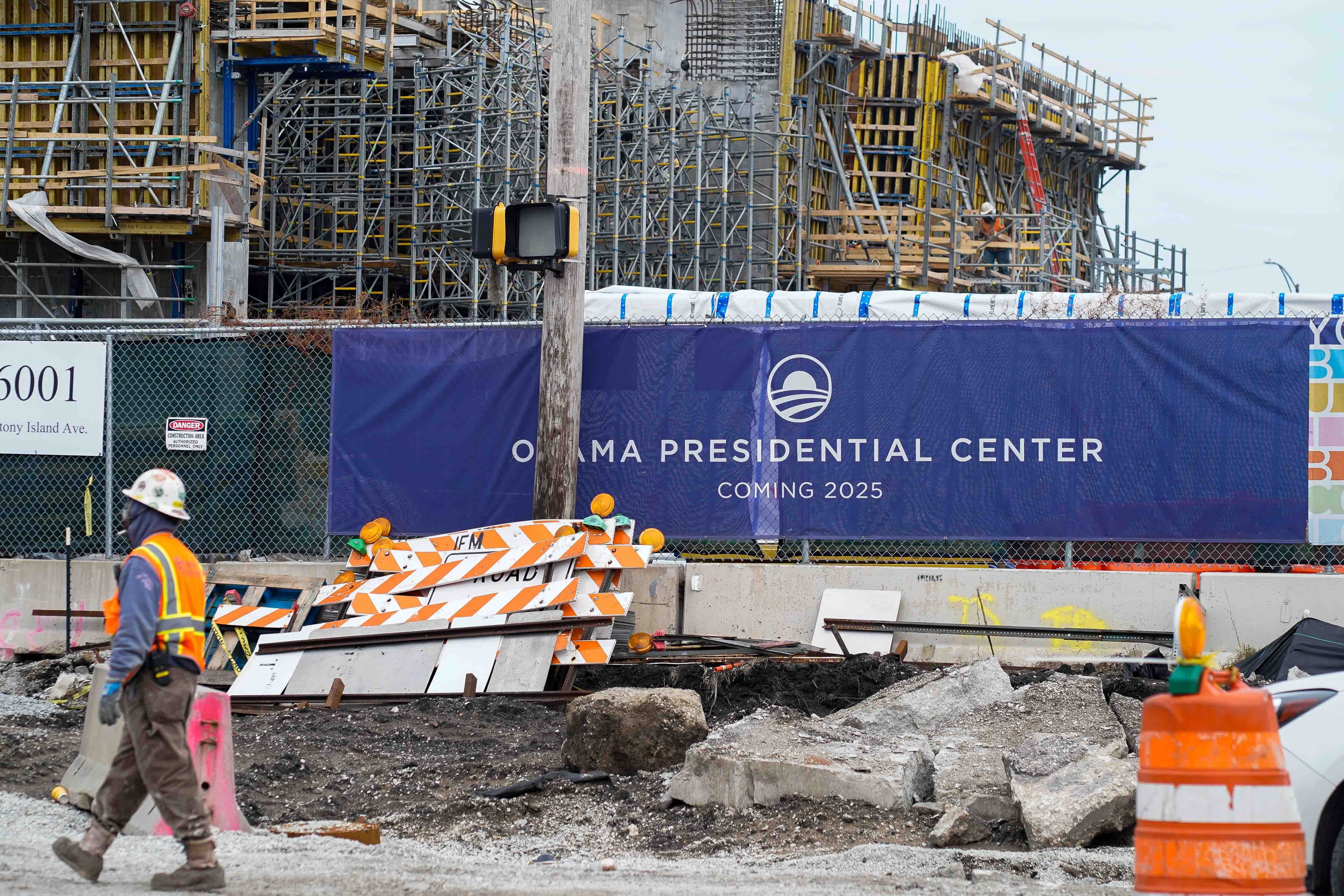 Worker in construction clothes in front of blue sign at construction site saying "Obama Presidential Center."