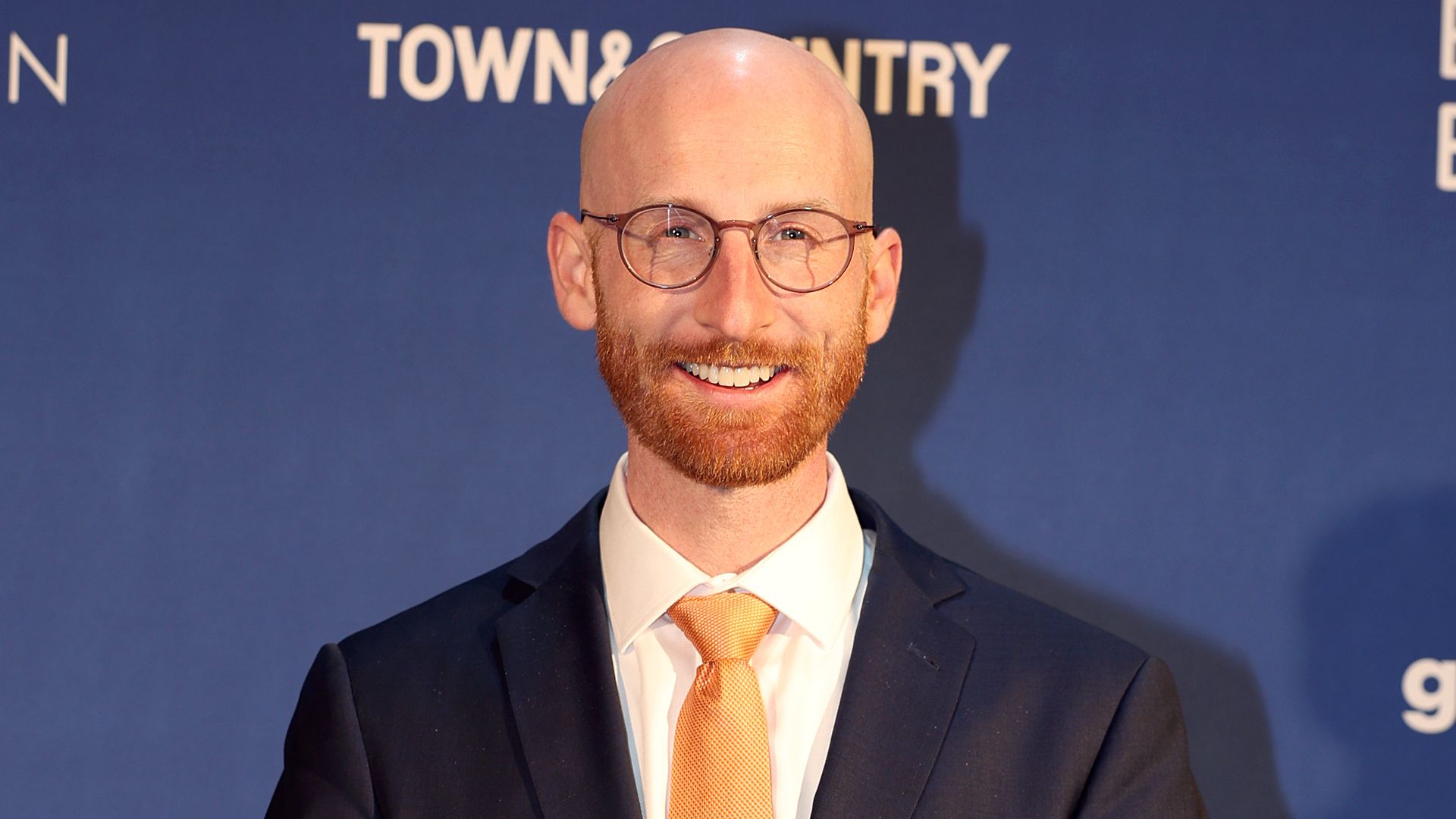Derek Kitchen stands in a black suit over a blue backdrop.