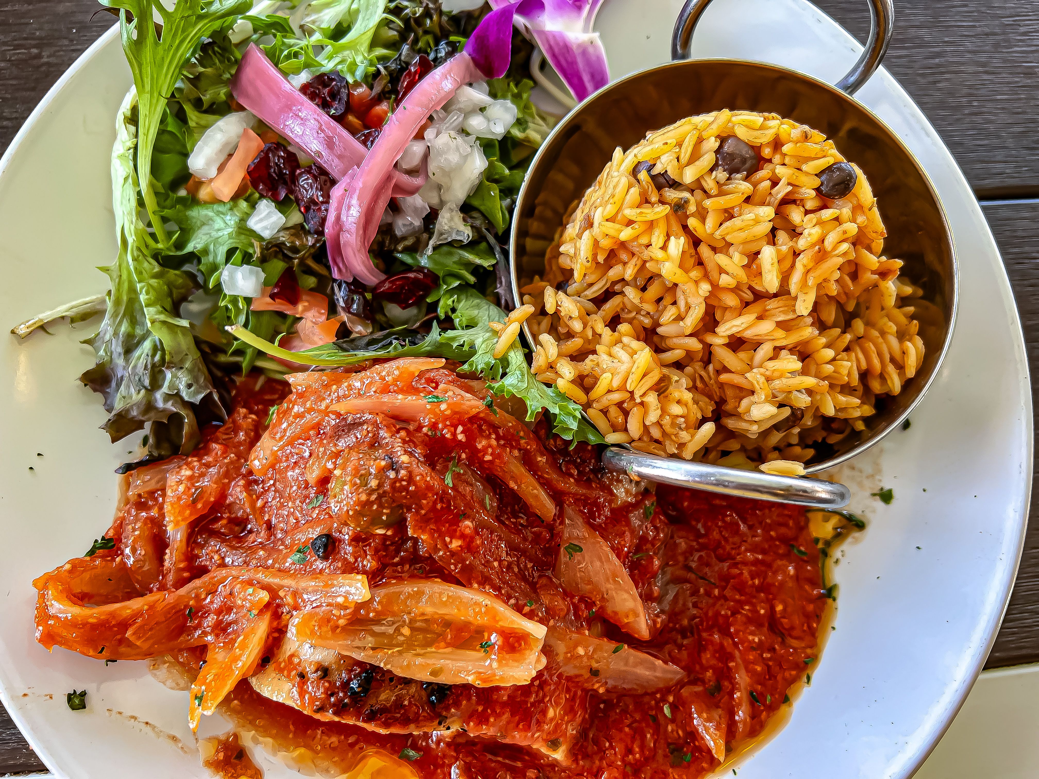 A dish consisting of fish covered in red sauce, rice and side salad.