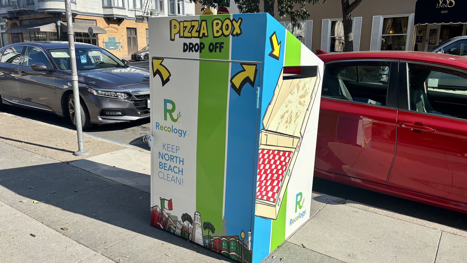 A colorful pizza box drop-off bin on a city sidewalk next to parked cars, with blue, green, and white colors and illustrations, labeled "Recology" and "Keep North Beach Clean!"