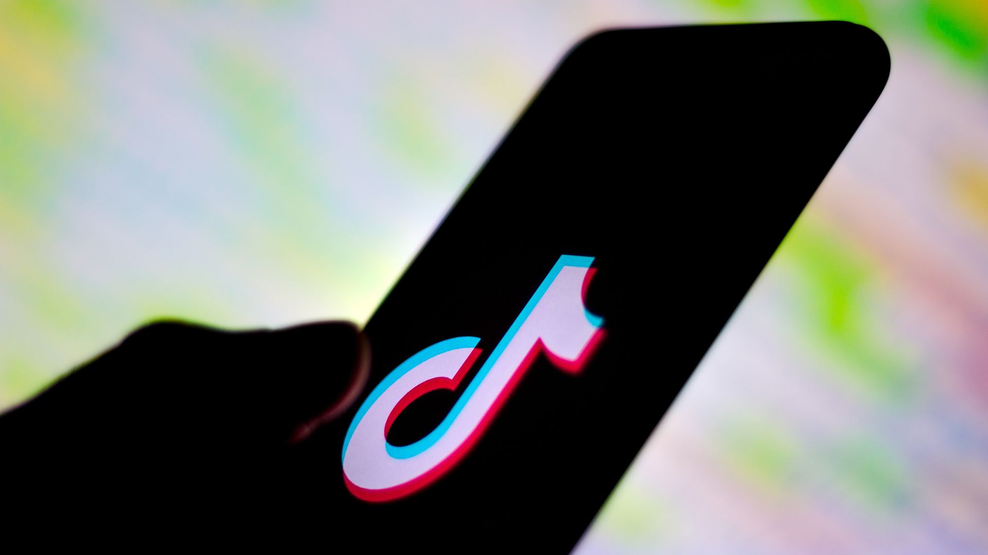 A photo illustration of a hand holding a smartphone with the TikTok logo on the screen.