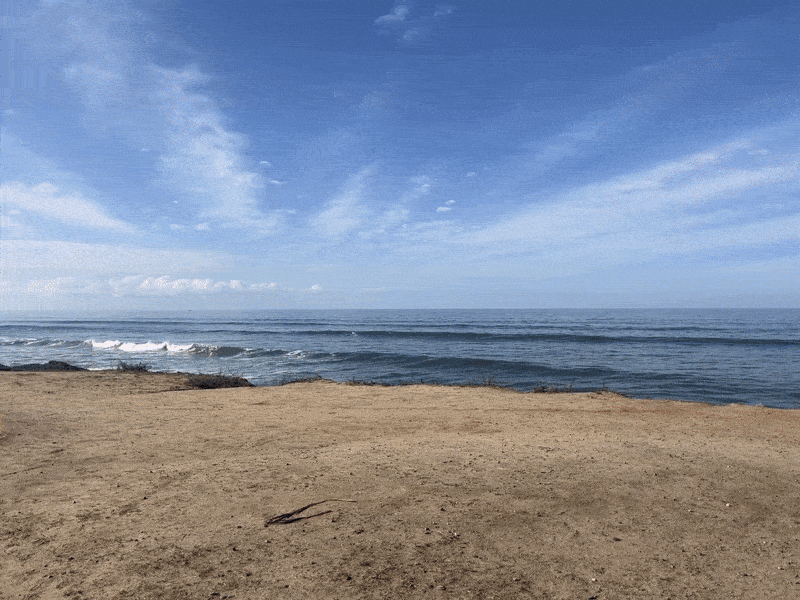 A video panning across cliffs on the ocean with waves crashing and a group of four people doing yoga. 