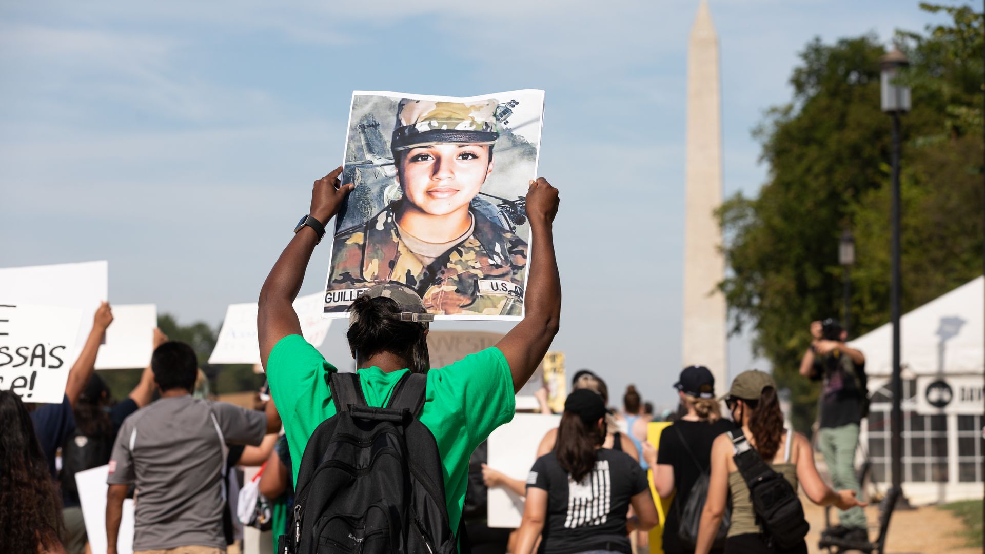 Photo of a person holding up a poster of Vanessa Guillén as they walk among a crowd of protesters