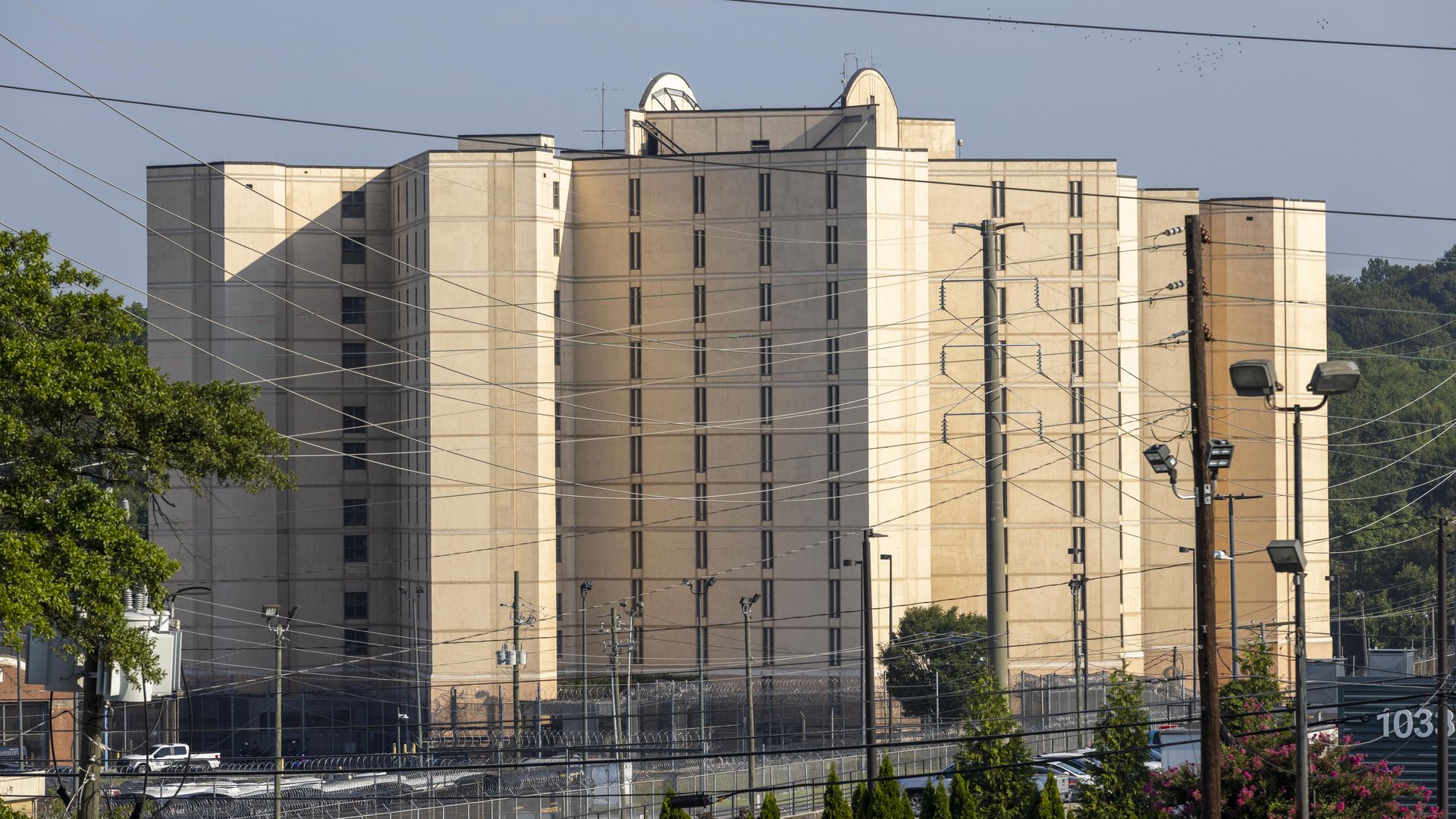 A large beige building with vertical, narrow windows and several towers sits behind power lines and utility poles. 