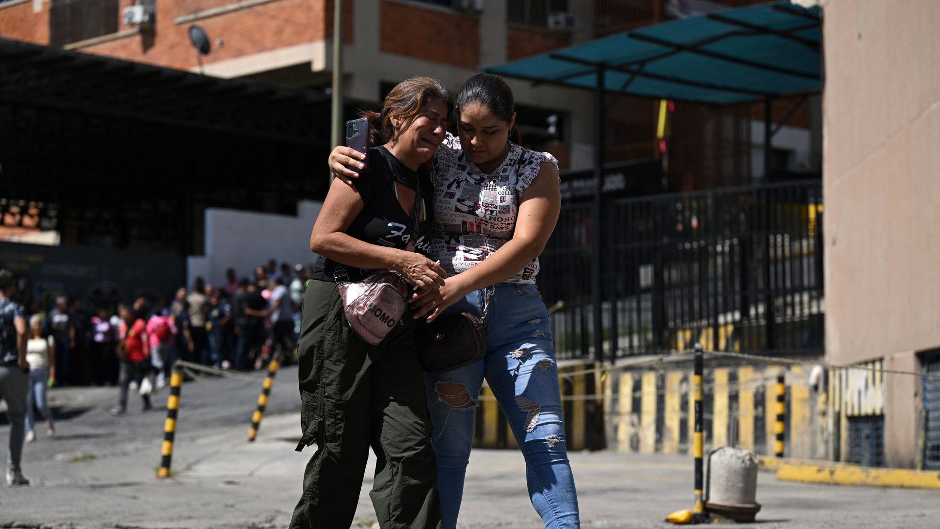 Two women are walkingdown the street in Caracas, Venezuela. One woman is comforting the other woman who is crying. 