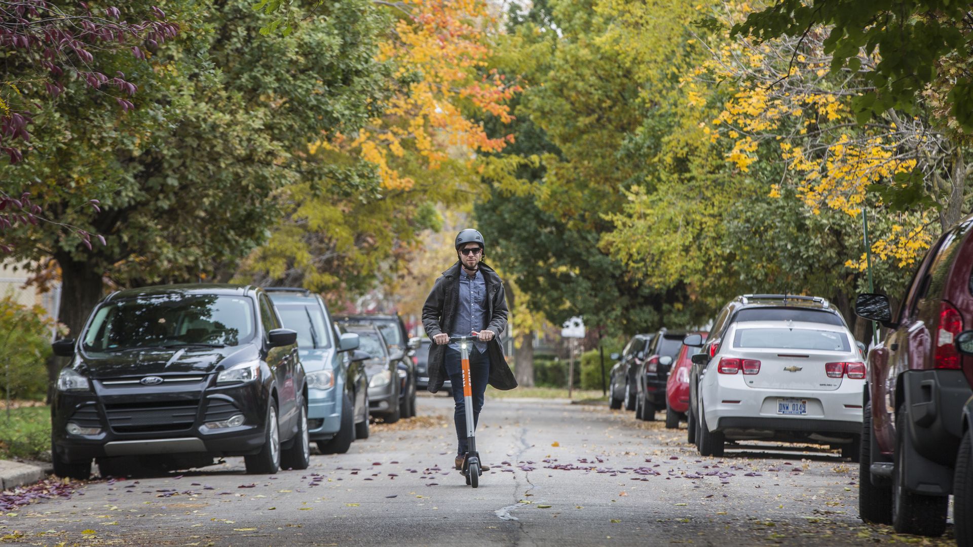 image of a man riding a scooter on a car-lined street