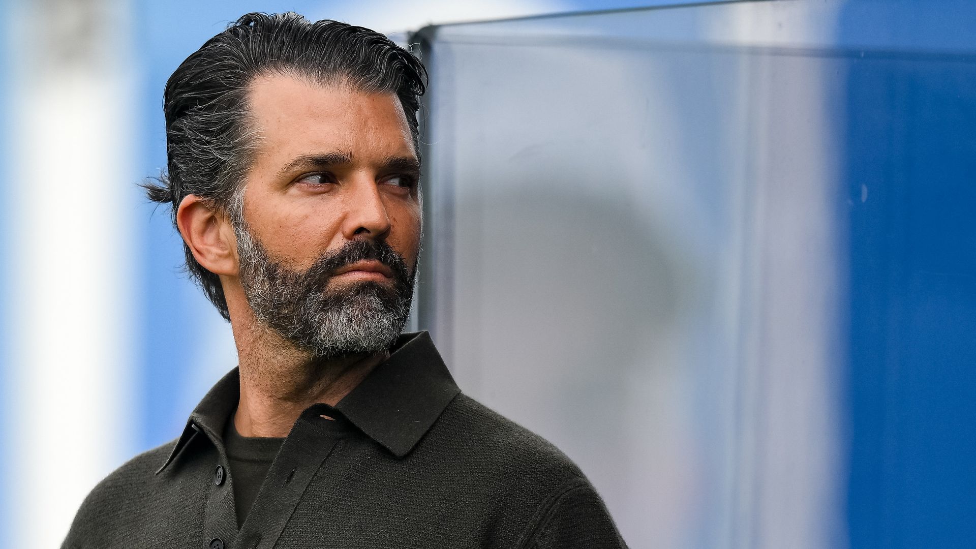 Donald Trump Jr. stands at the left of the frame looking left over his shoulder
