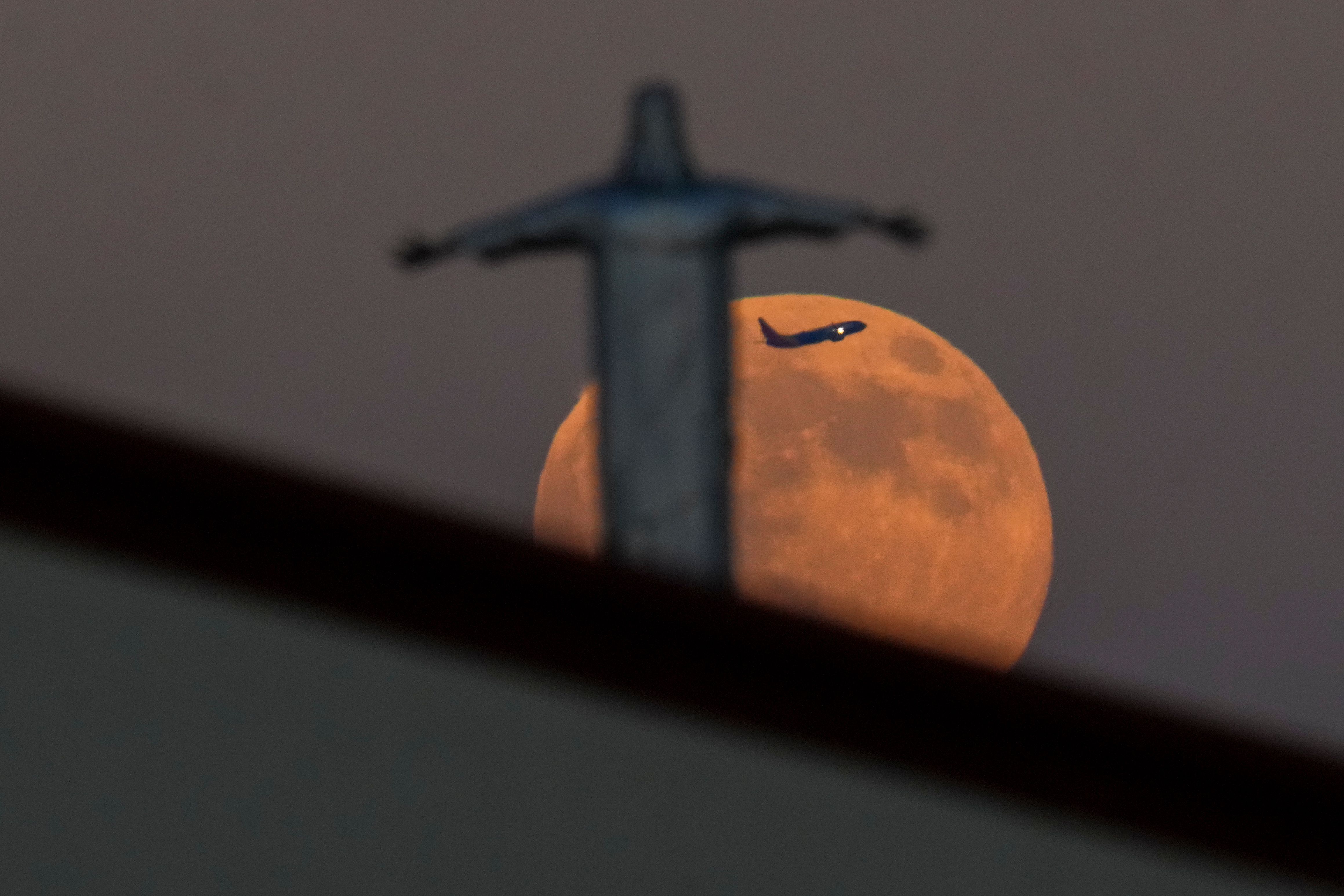A Southwest Airlines plane appears between the Harvest Supermoon and a statue of Jesus Christ atop Iglesia Luterana Santa Maria de Guadalupe as it takes off from Dallas Love Field Airport