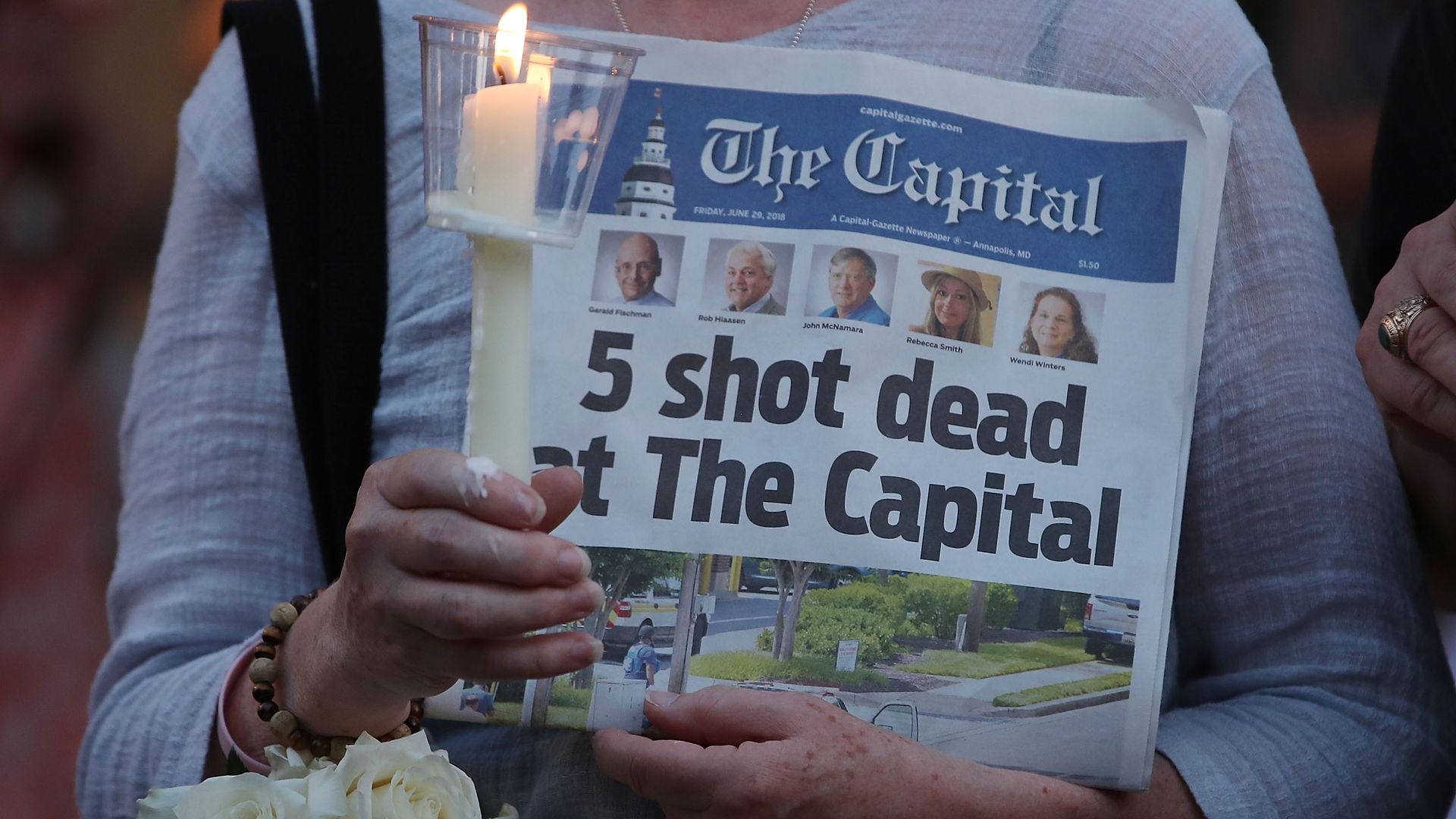 A women holds a newspaper and candle. 