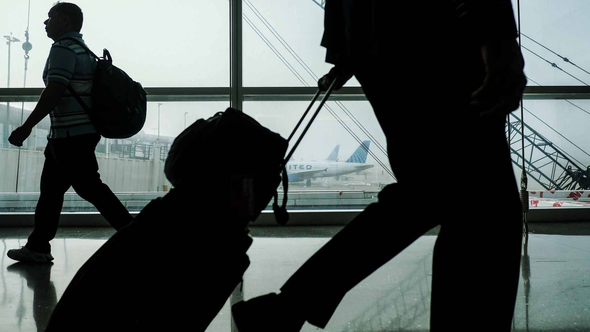 Image shows two travelers walking with suitcases and backpacks.