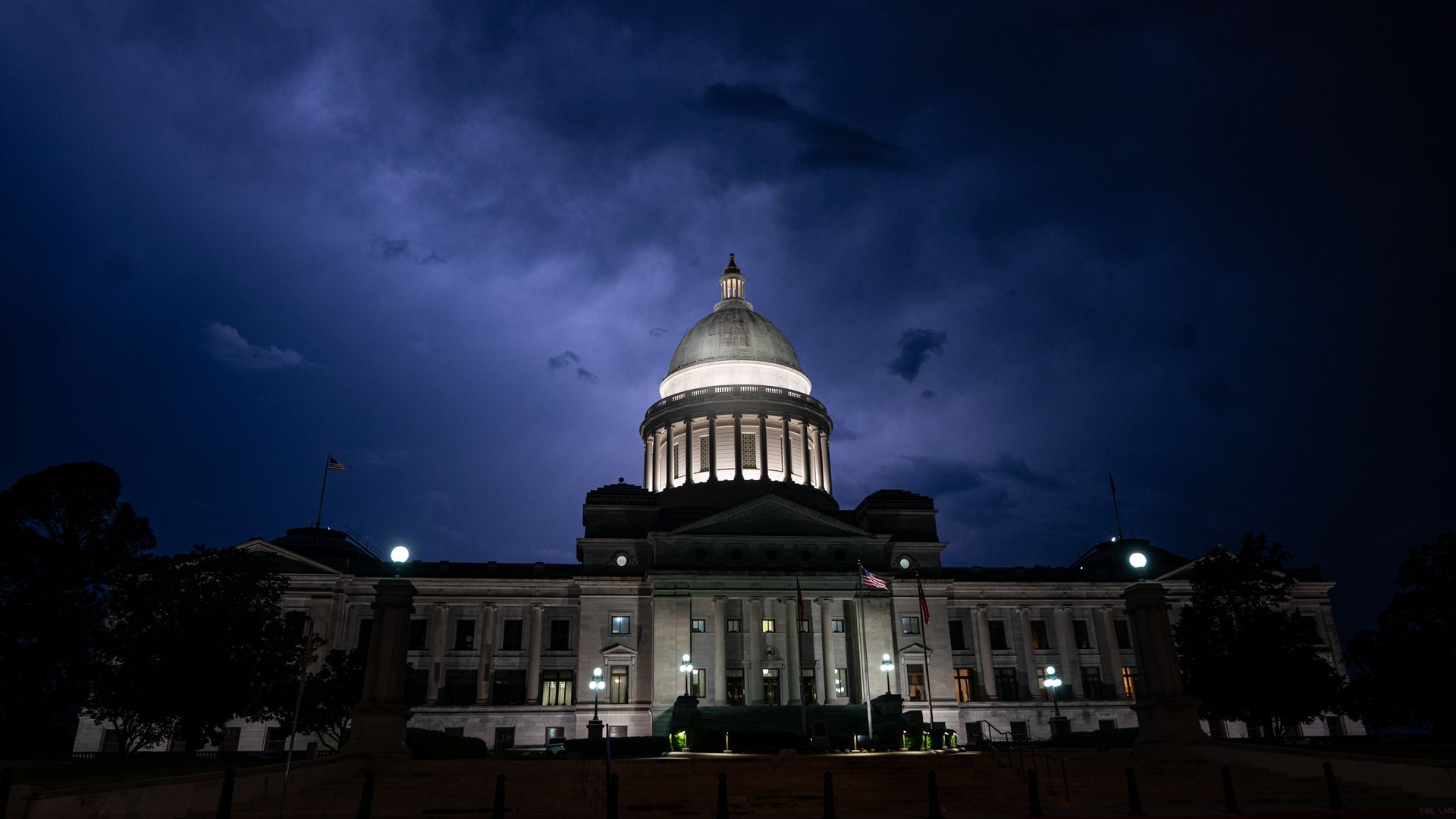 The Capitol building in Little Rock, Arkansas, is lit up at night time with a cloudy blue sky in the background.