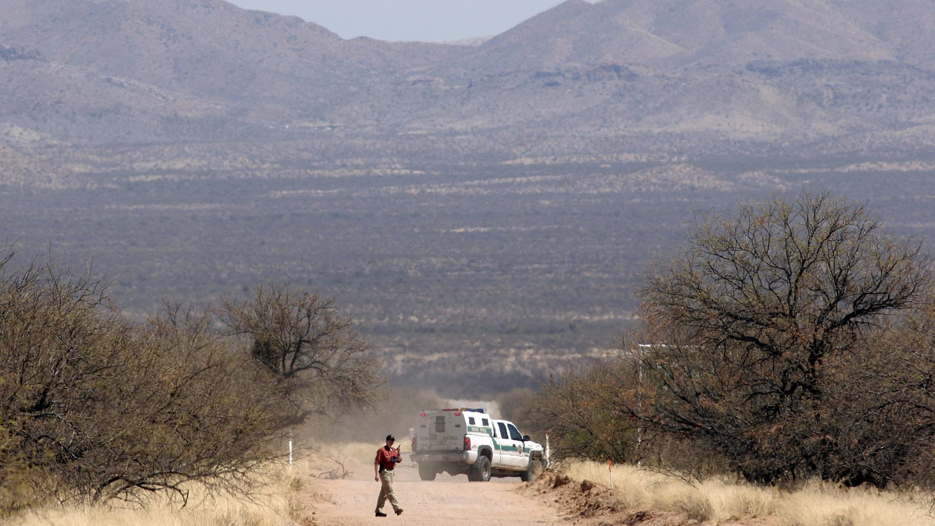 A mountain in the background with a car on the desert in the foreground. 