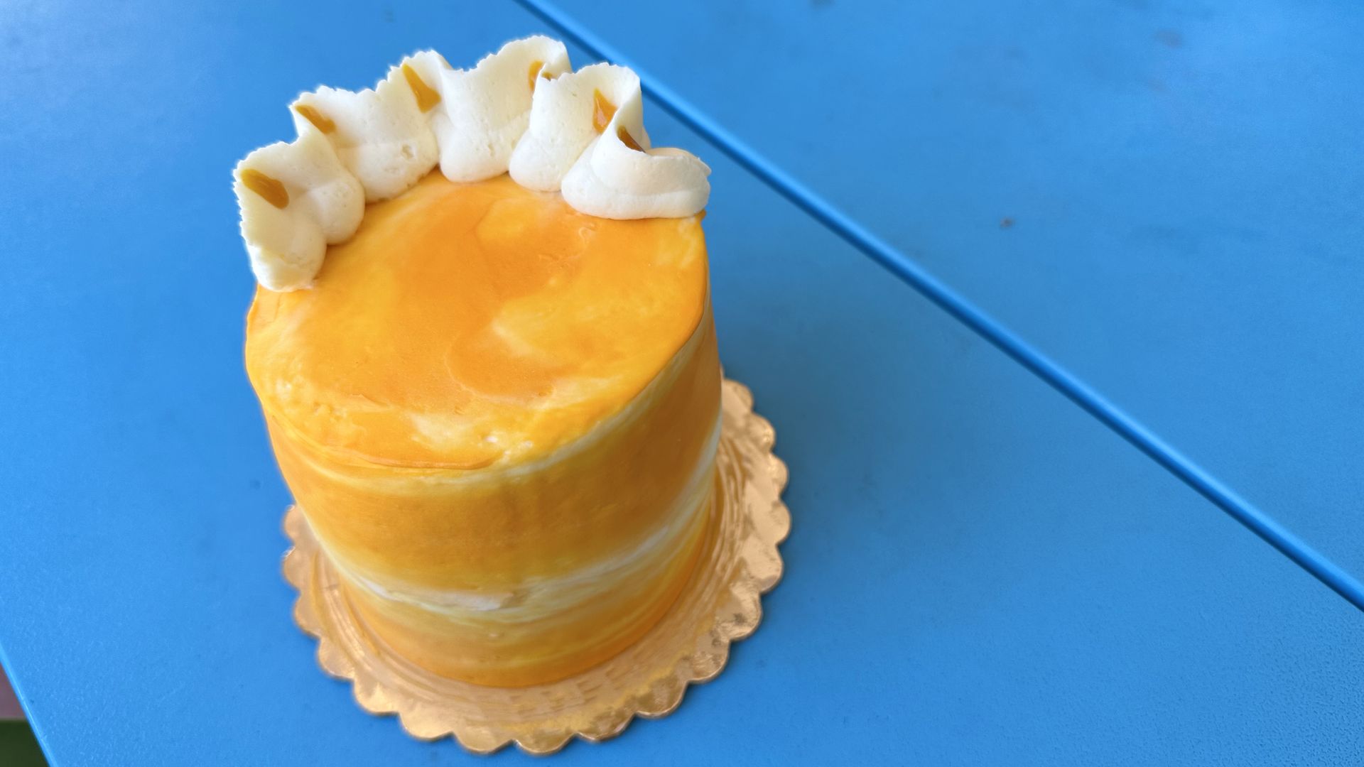 Photo shows an orange cake on a blue picnic table.