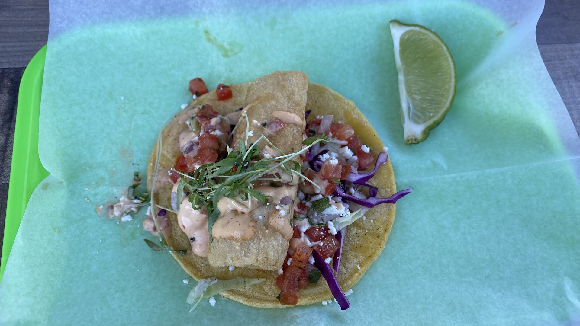 A piece of breaded fish in a taco with greens, sauce and pico de gallo. 