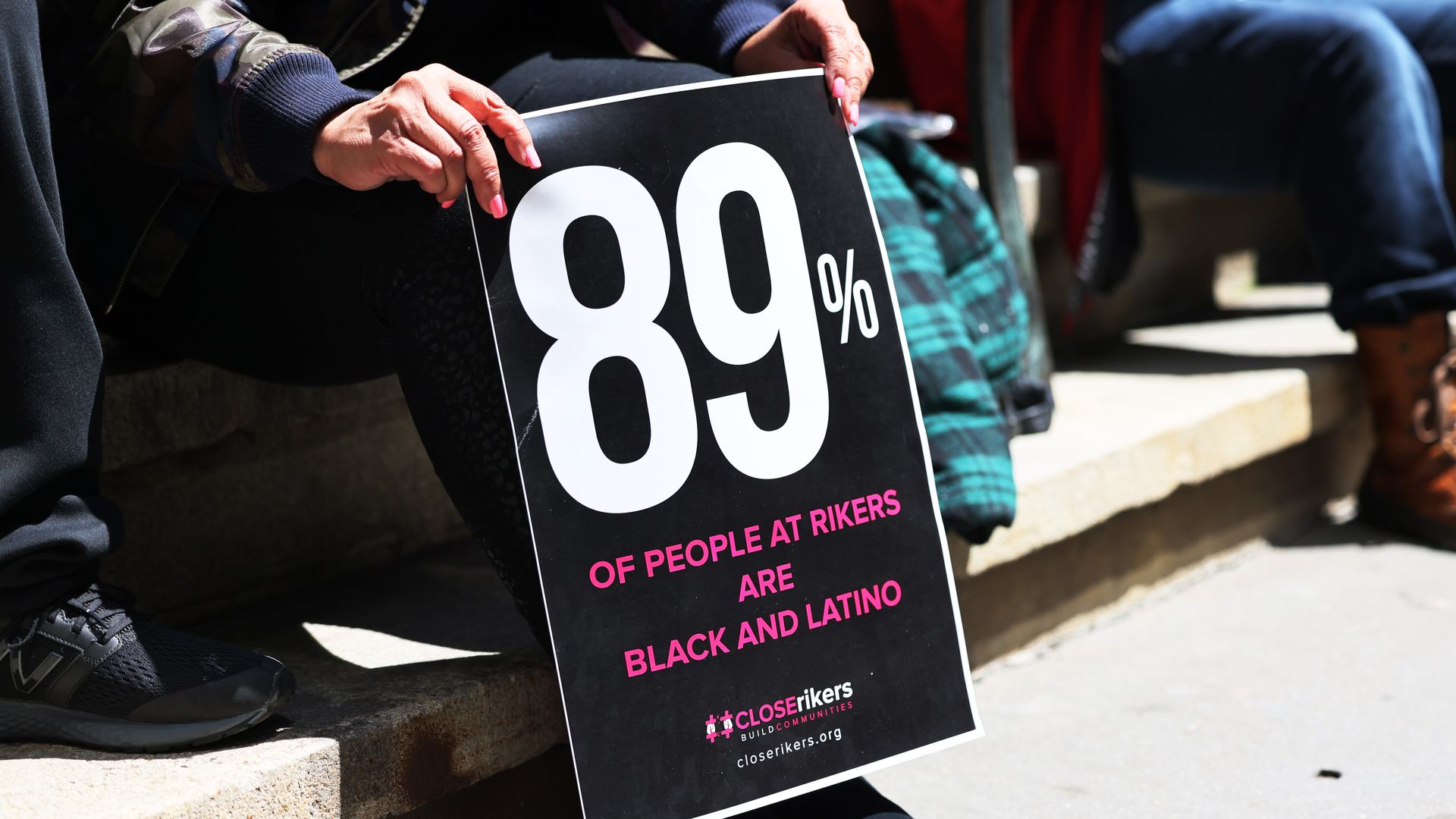 Photo of a person holding a sign that says "89% of people at Rikers are Black and Latino"