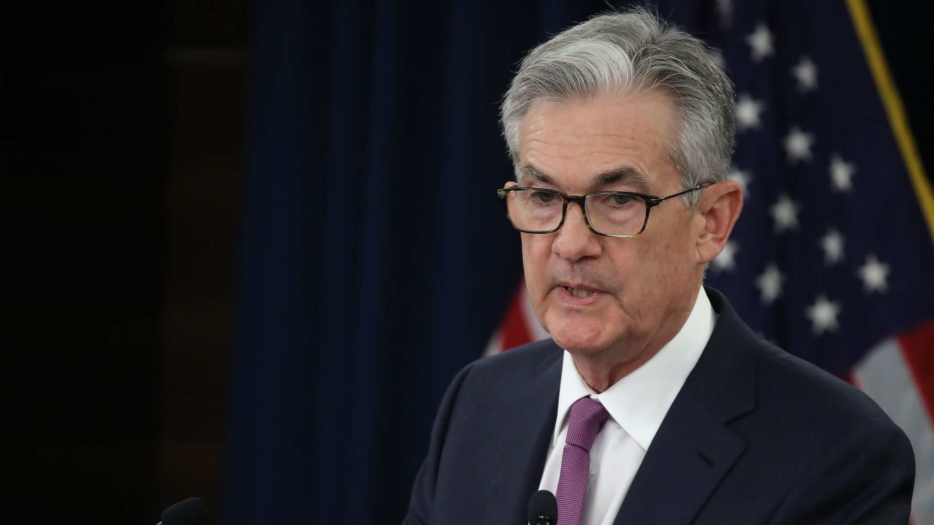 In this image, Powell stands in a suit and speaks while holding papers.
