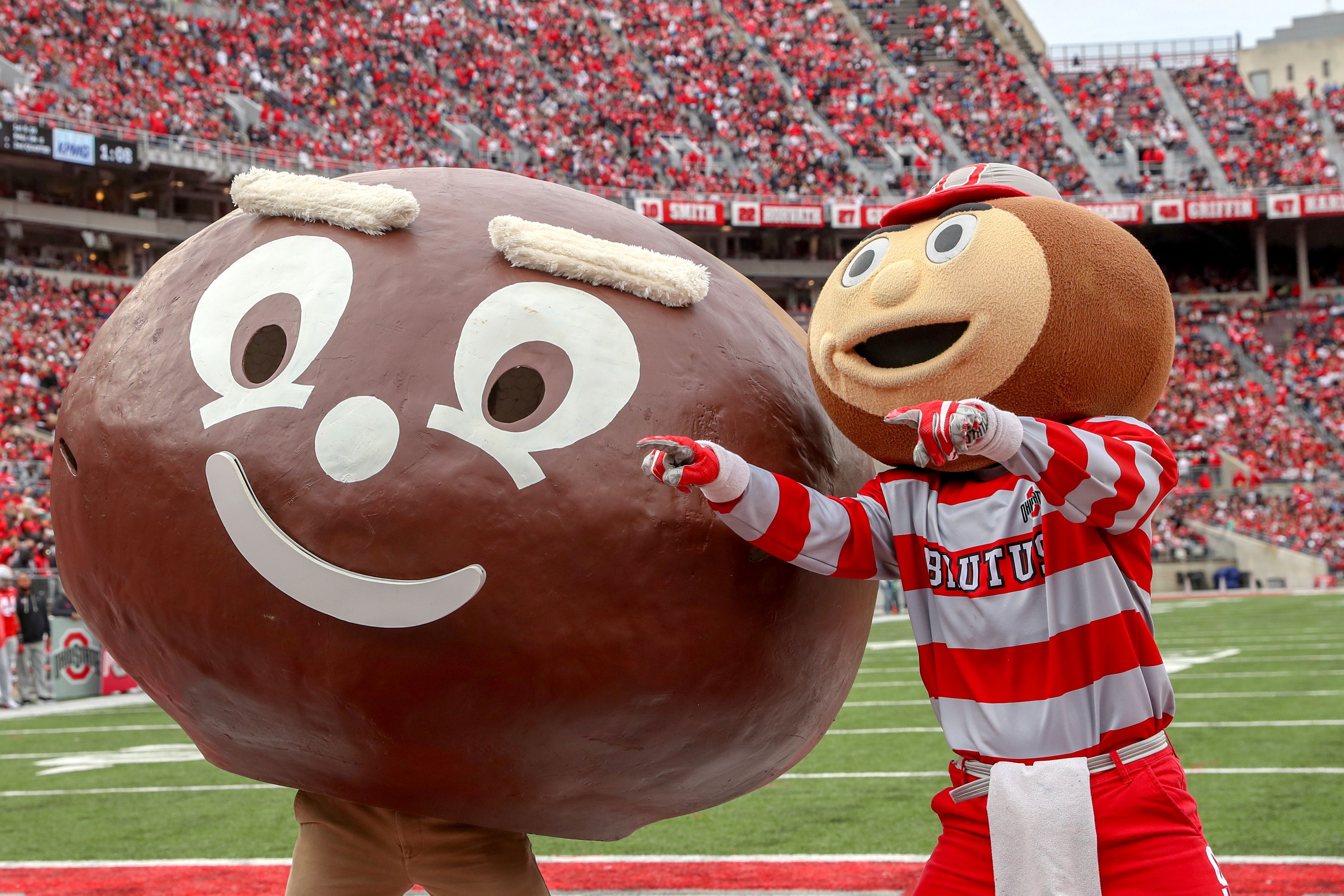 Two versions of Brutus buckeye — from the '60s and today — stand on the field at Ohio Stadium