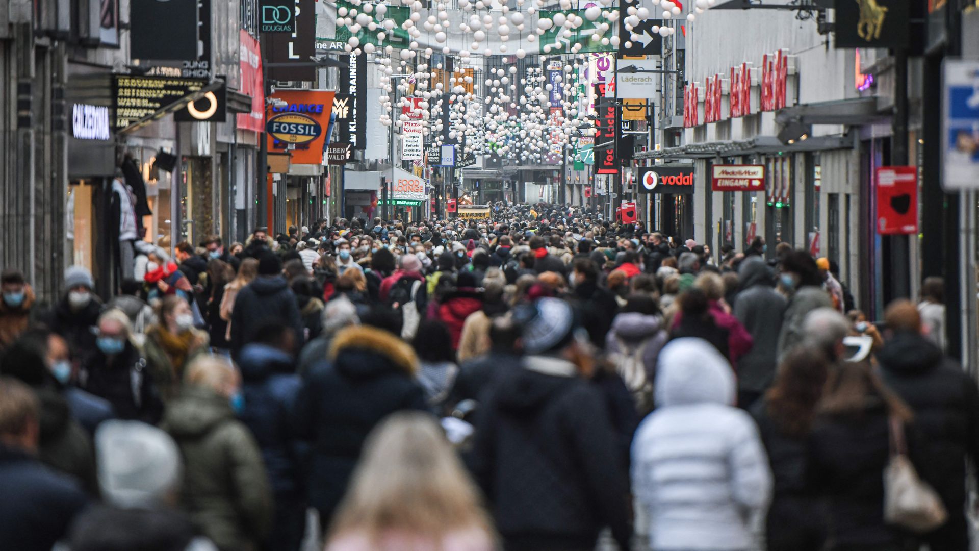 People are seen wearing face masks as they walk in a pedestrian street among shops and Christmas decorations in the city of Cologne, western Germany, on December 18, 2021. 