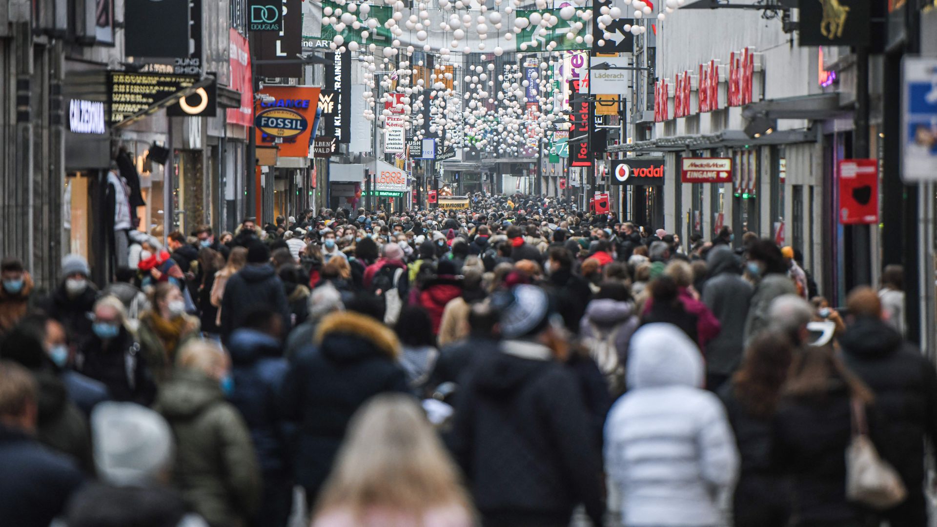 People are seen wearing face masks as they walk in a pedestrian street among shops and Christmas decorations in the city of Cologne, western Germany, on December 18, 2021.
