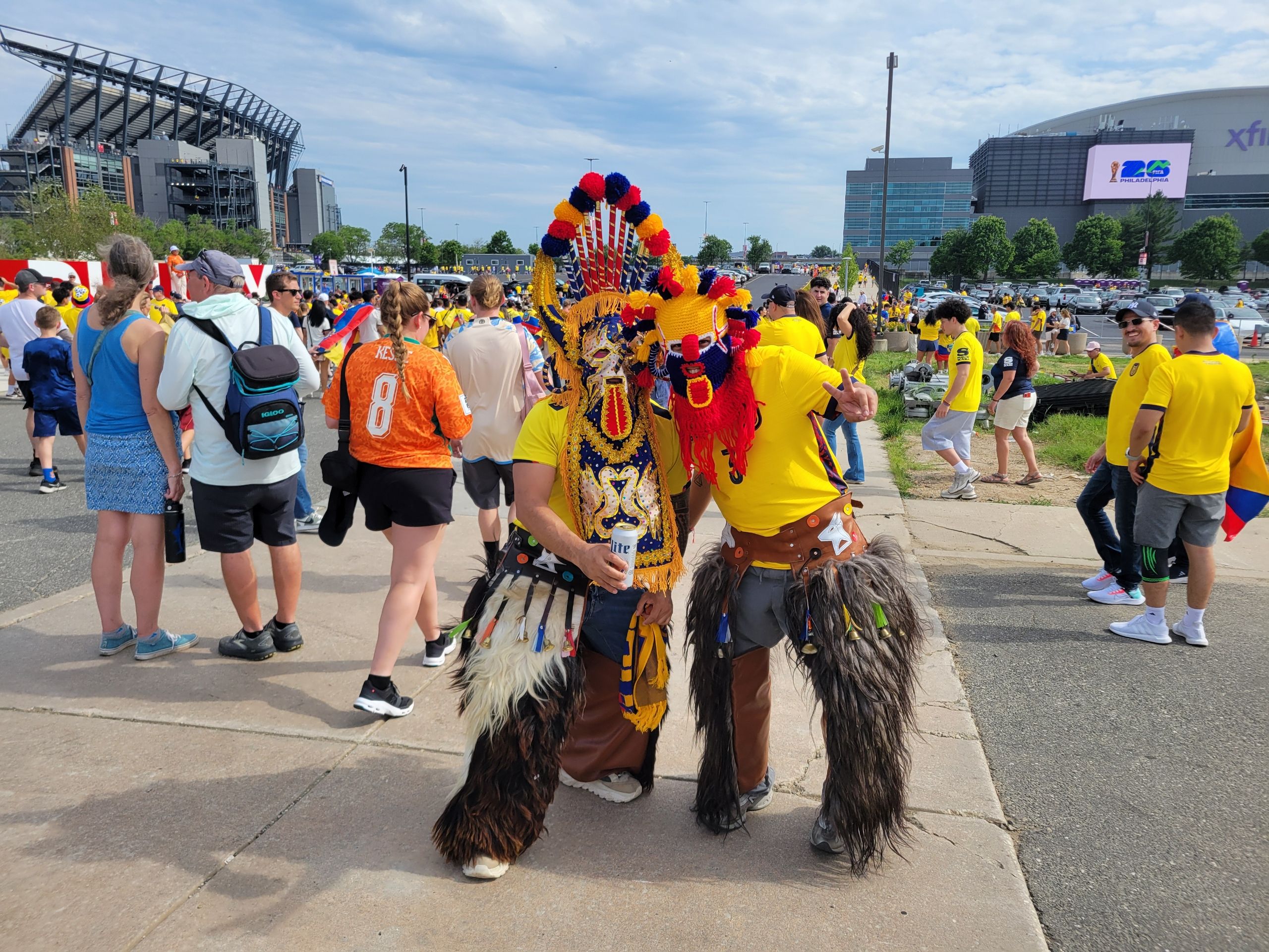 Ecuador fans decked out in masks and yellow shirts pose near a stadium.