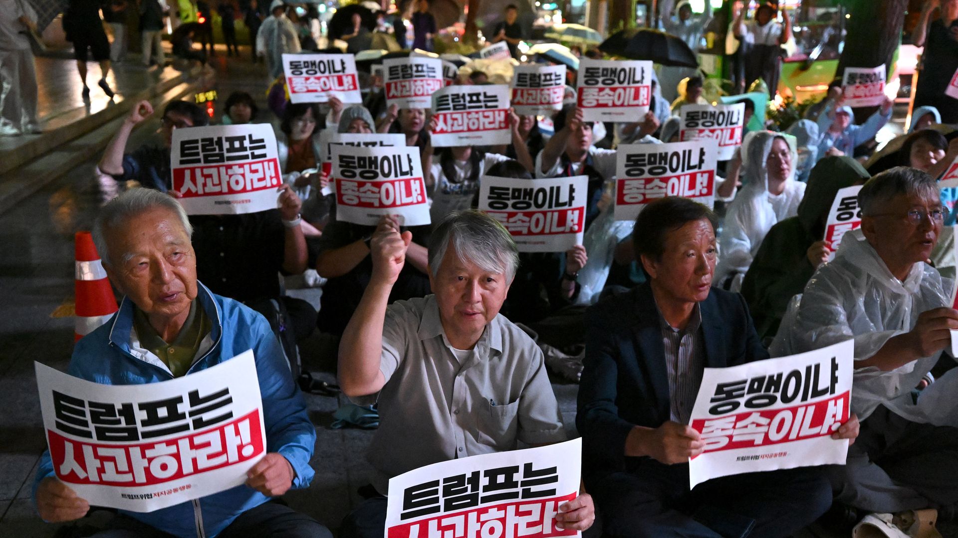 South Koreans, seated on the ground, holding signs that read in Korean "Trump, apologize!"