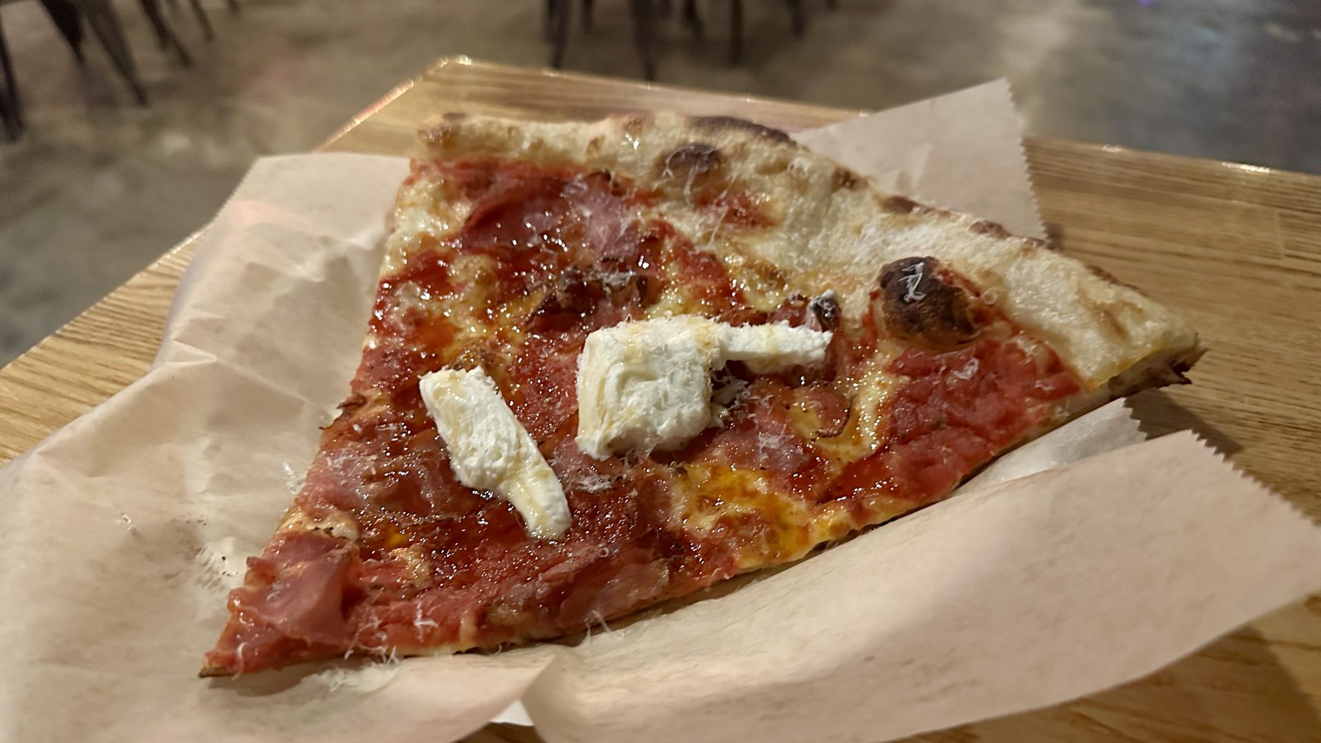 A slice of pizza with red sauce, coppa, burrata and hot honey from Stevie's Famous, sitting on a bar table.