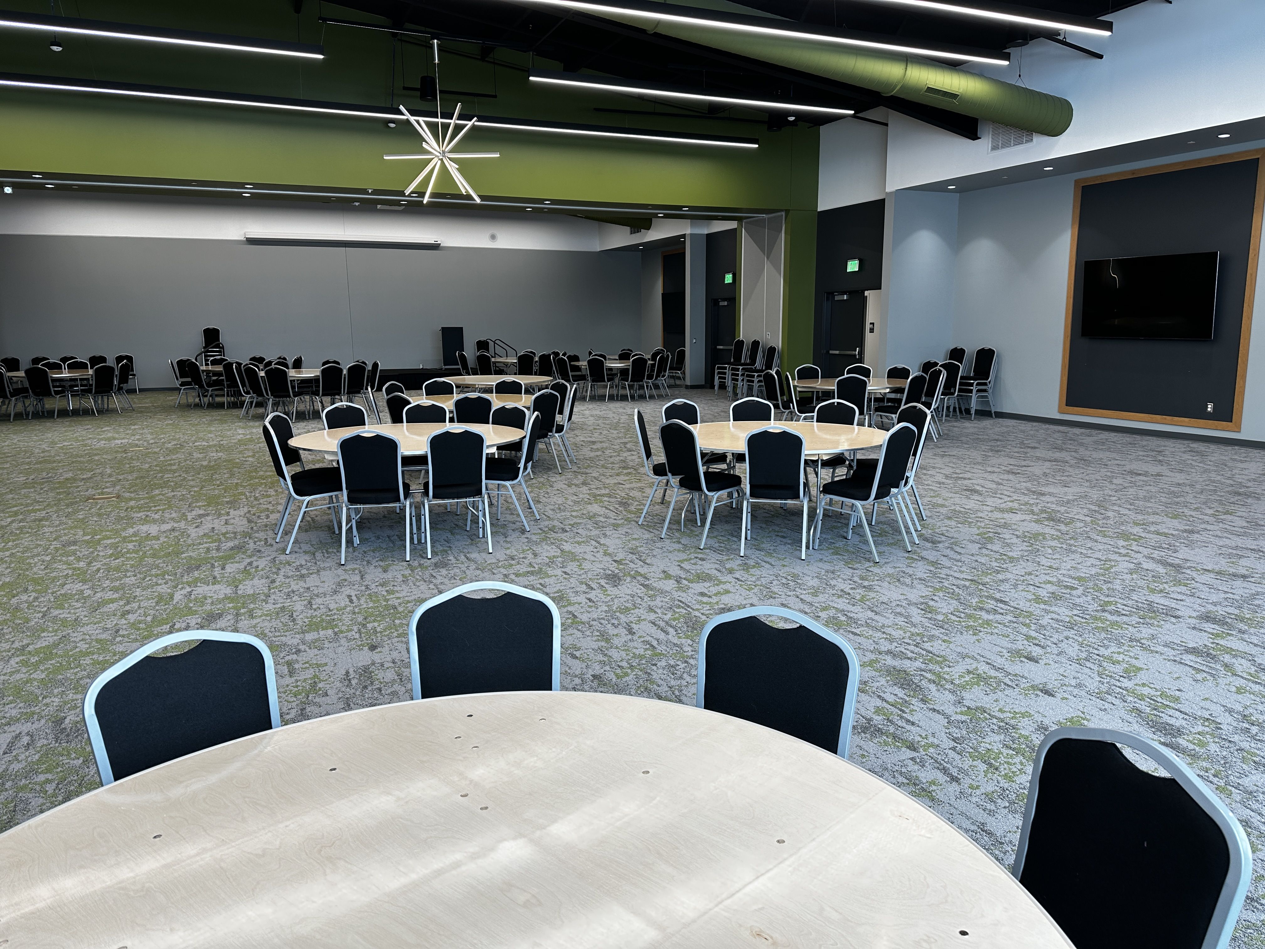A large banquet hall with tables and chairs and a green accent wall