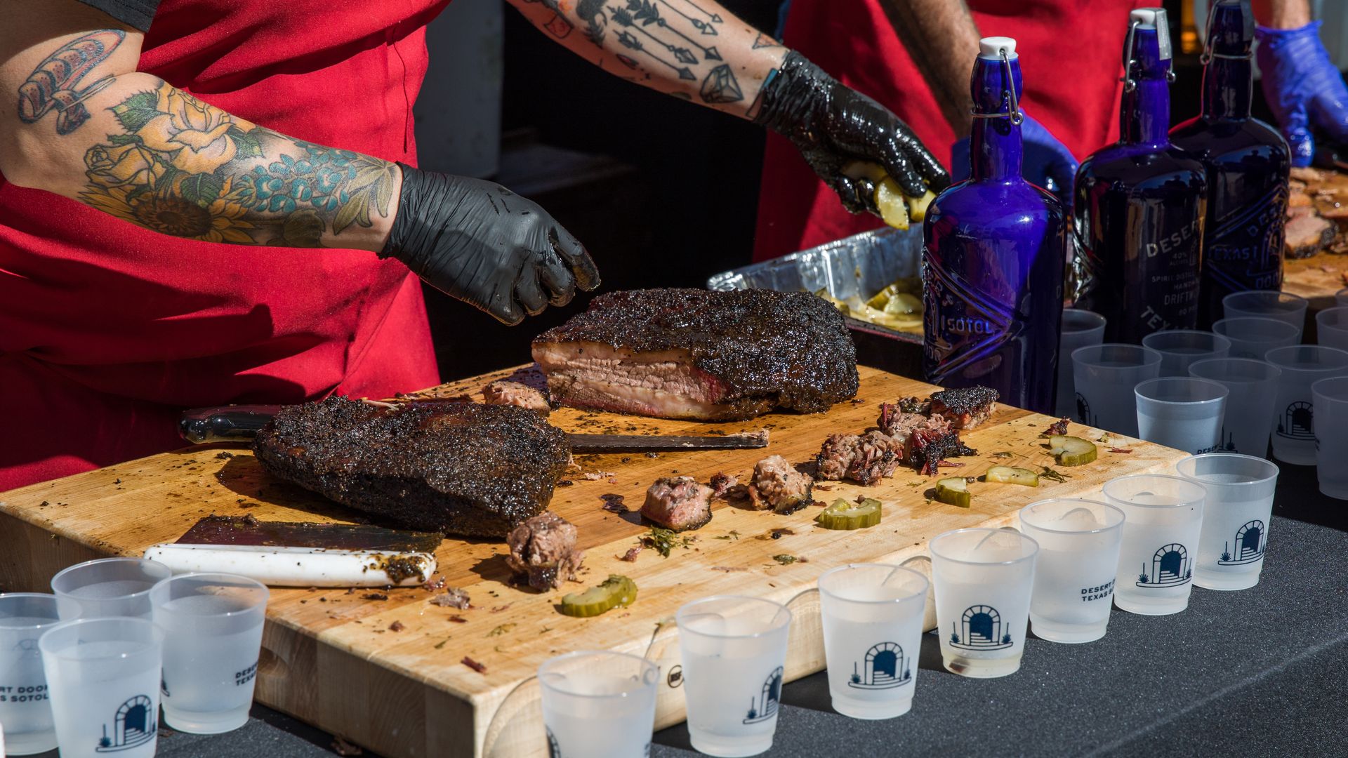 A photo of brisket being sliced on a cutting board surrounded by cups.