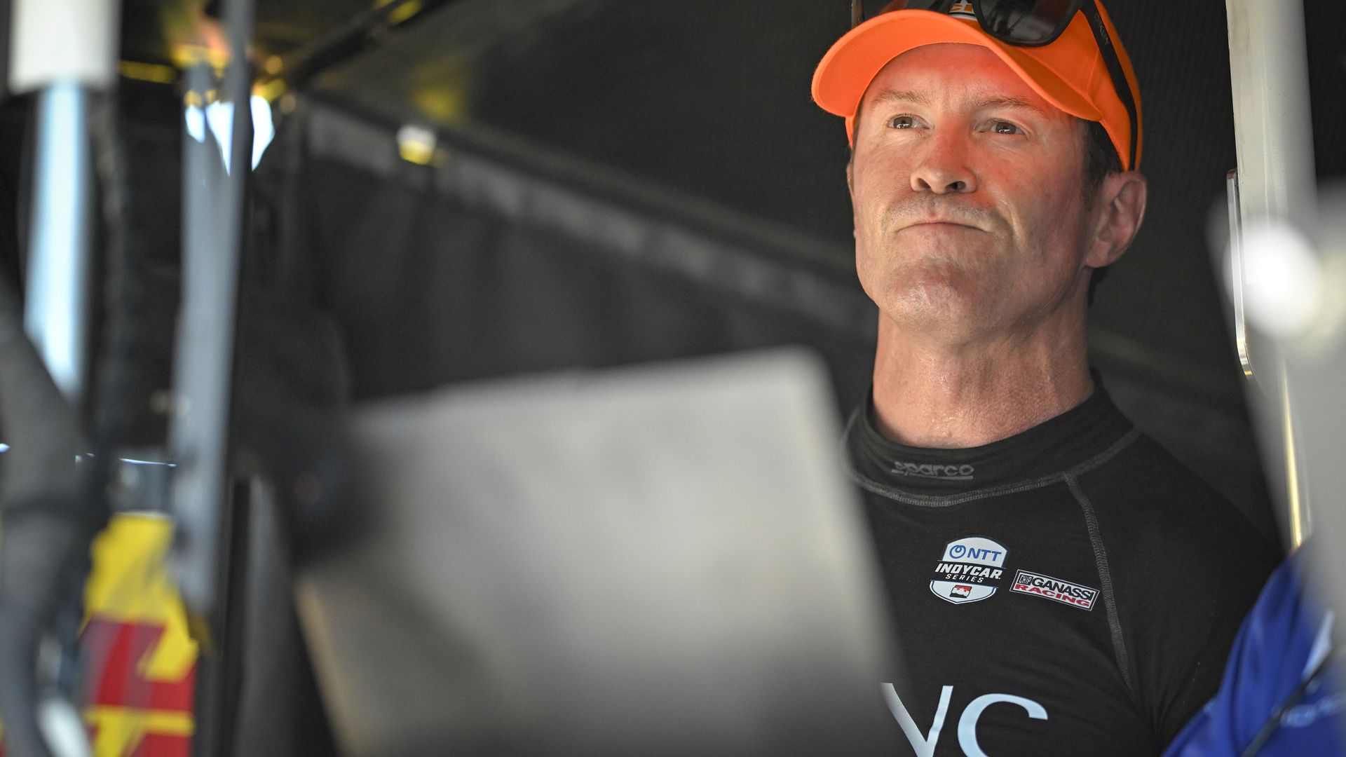 IndyCar driver Scott Dixon stares ahead in an orange cap. 