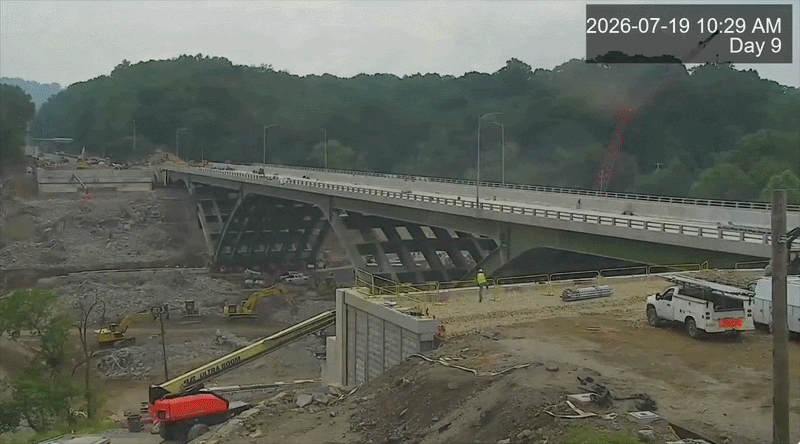A time lapse video of a highway bridge sliding into place over a ravine with green hills in the background.