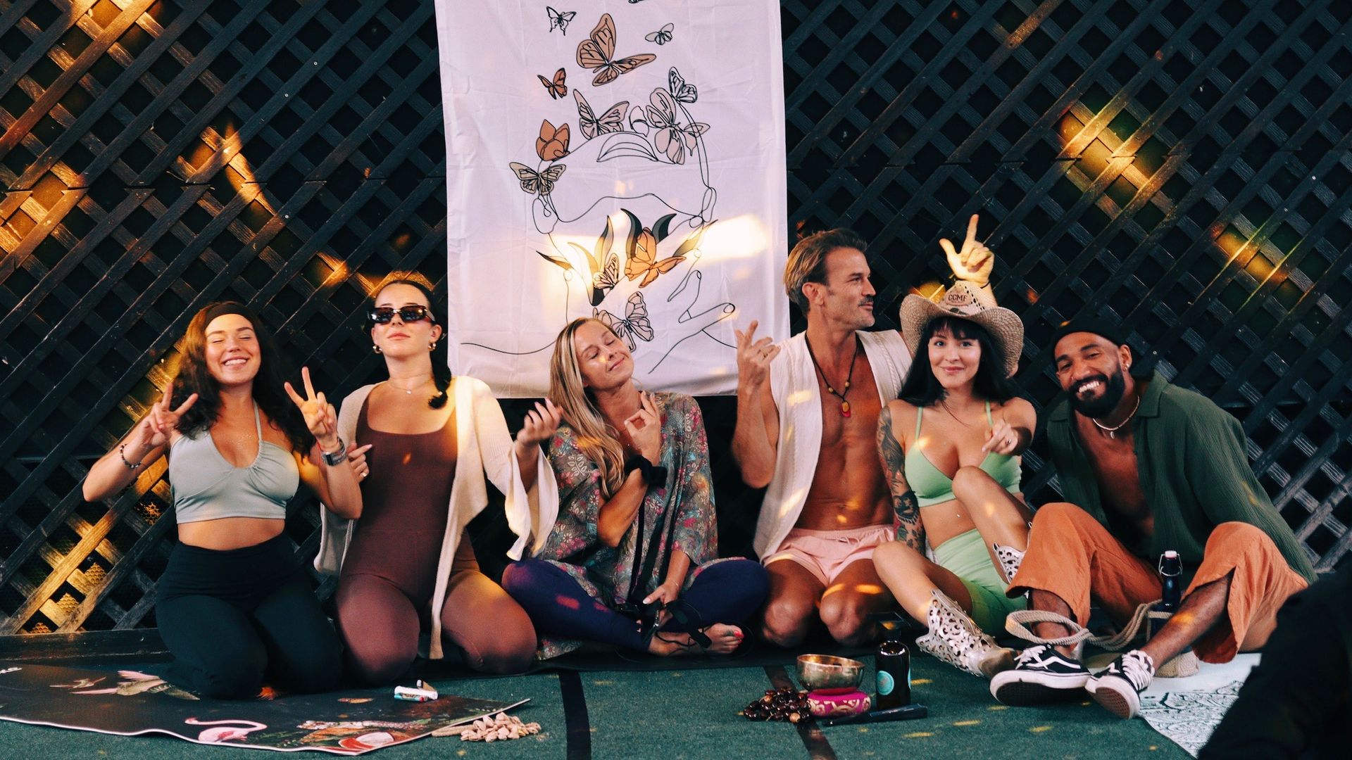 A group of friends in stretchy clothes and robes sits and gives peace signs with their hands. 