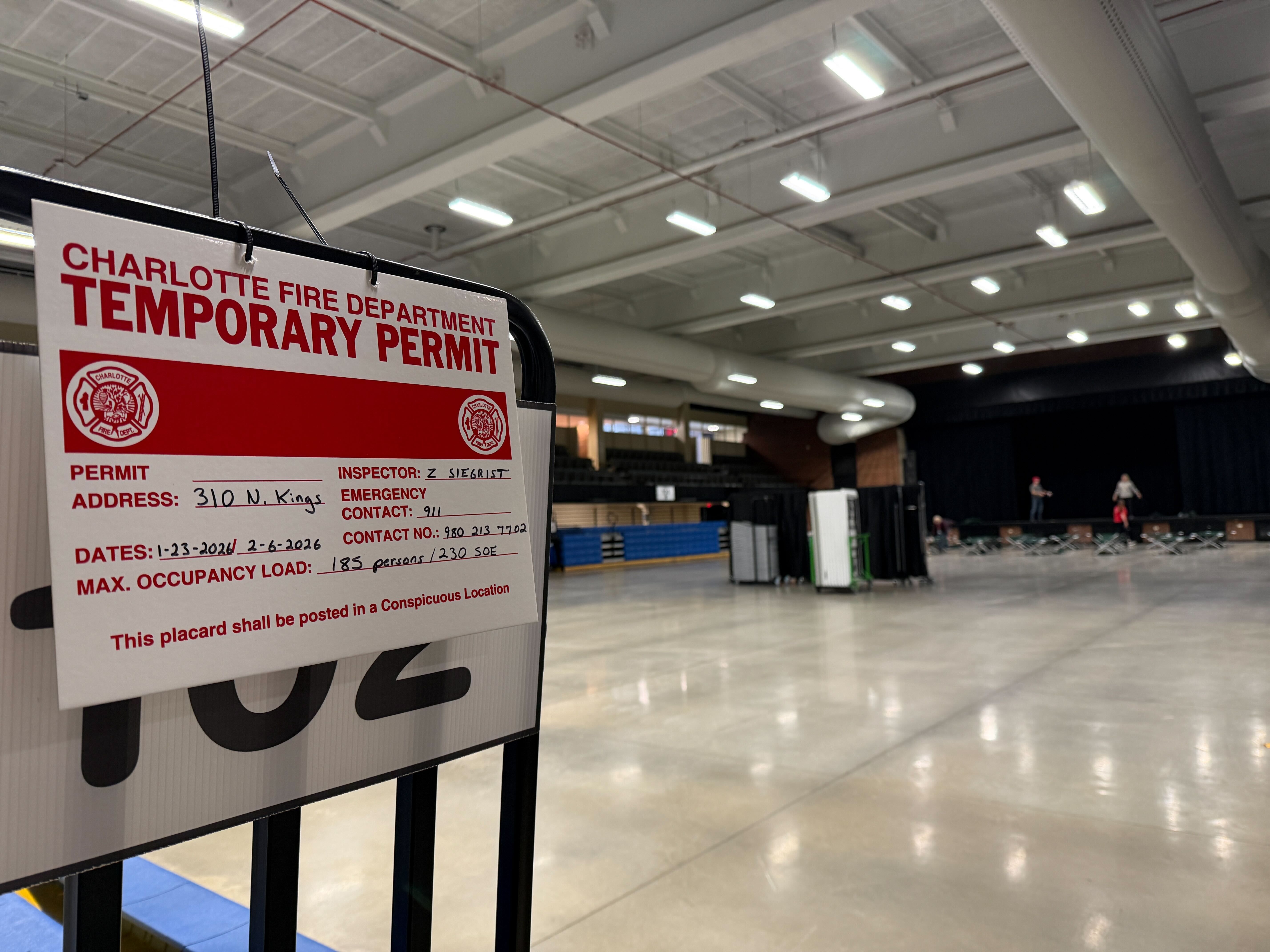 Charlotte Fire Department temporary permit posted in an indoor space with polished concrete floor, lighting, and a stage in the background with people setting up.