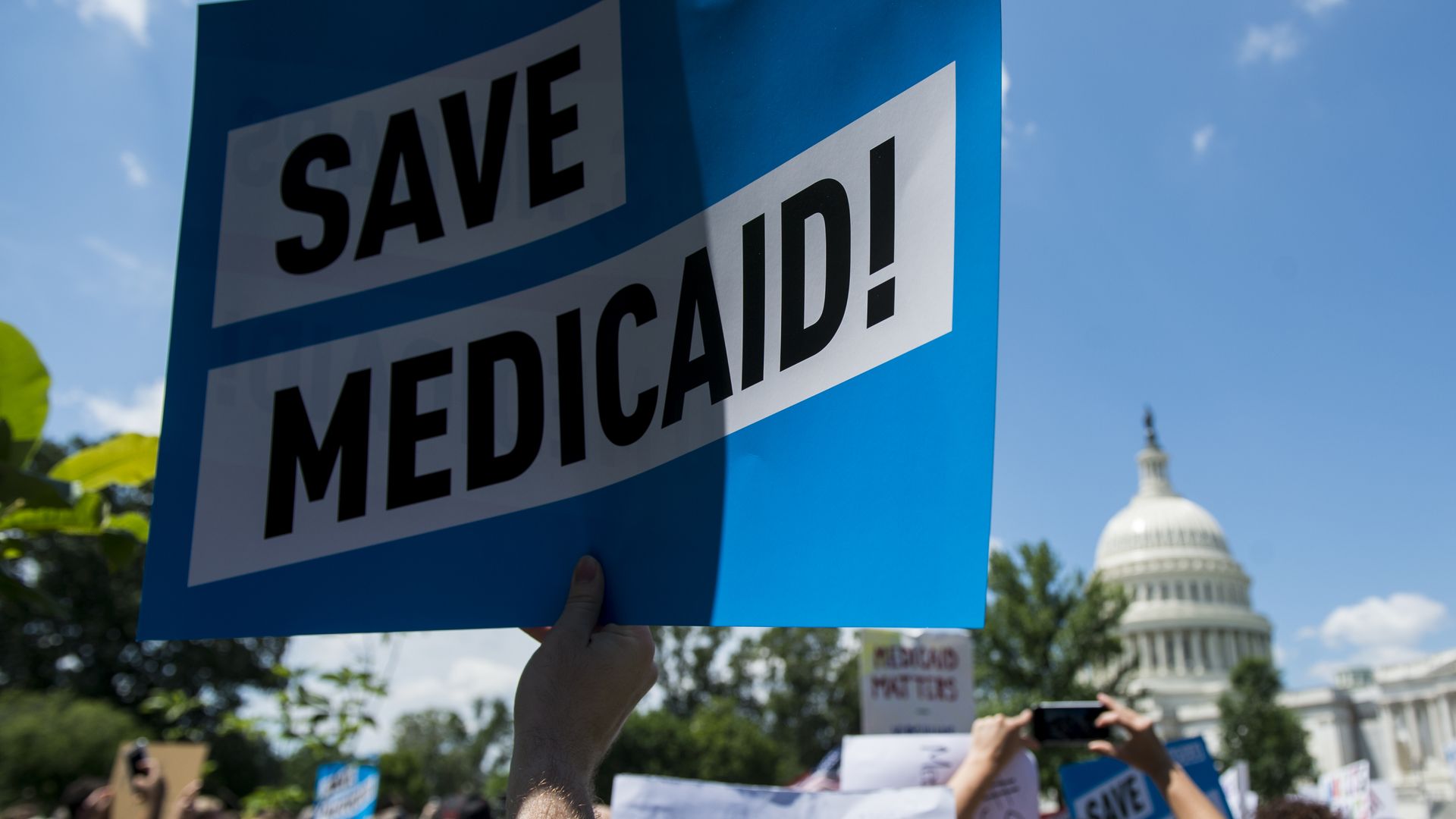 A person holds up a sign that says "Save Medicaid!"