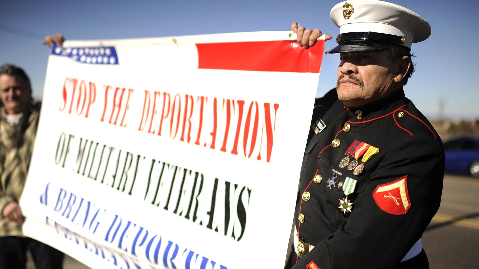 Retired U.S. Marine Manuel Valenzuela stands at the entrance of Buckley Air Force base in uniform and carrying a banner to protest the deportation of veterans.