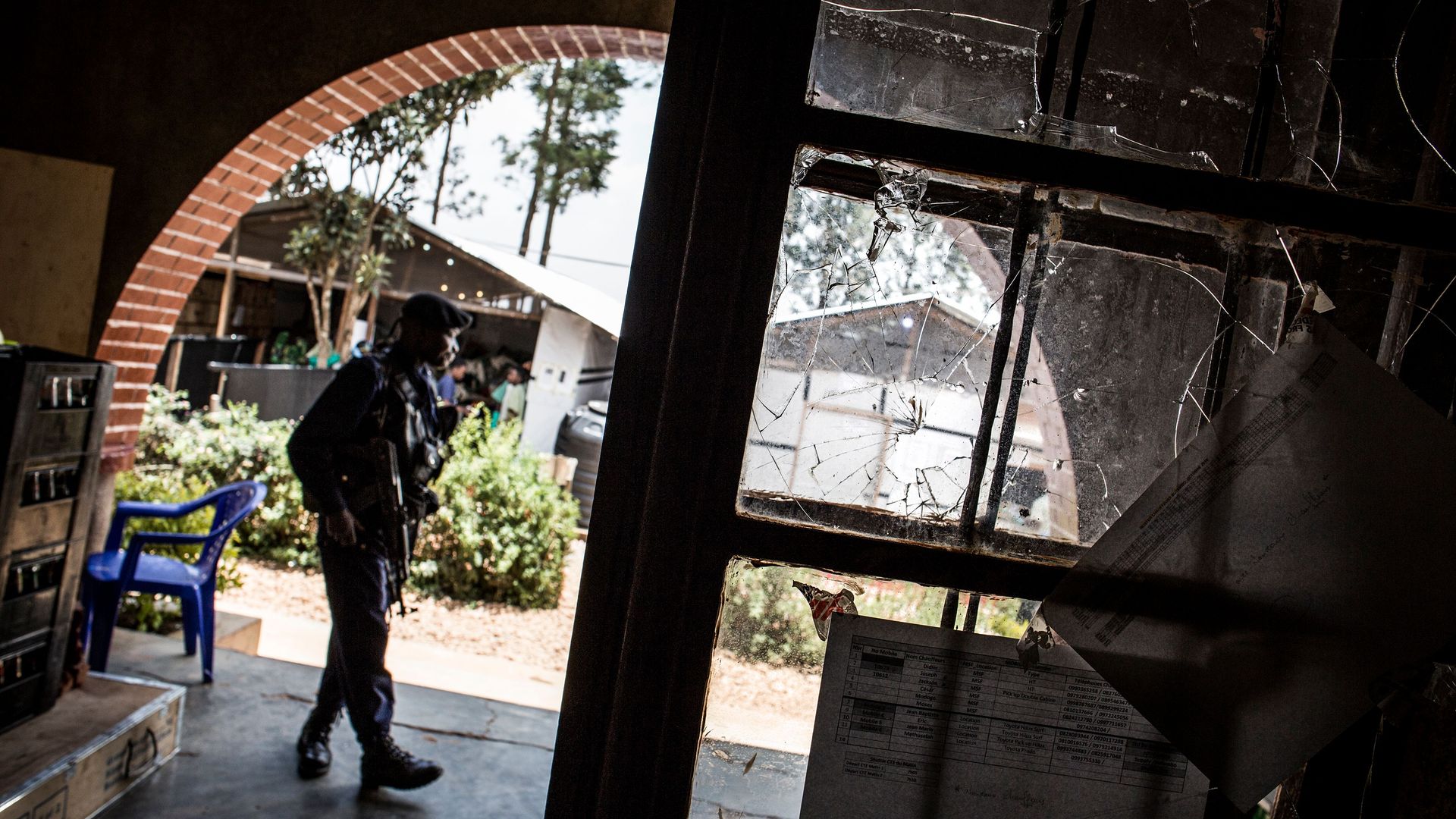 In this image, an armed police officer stands watch in an arched doorway that looks outside.