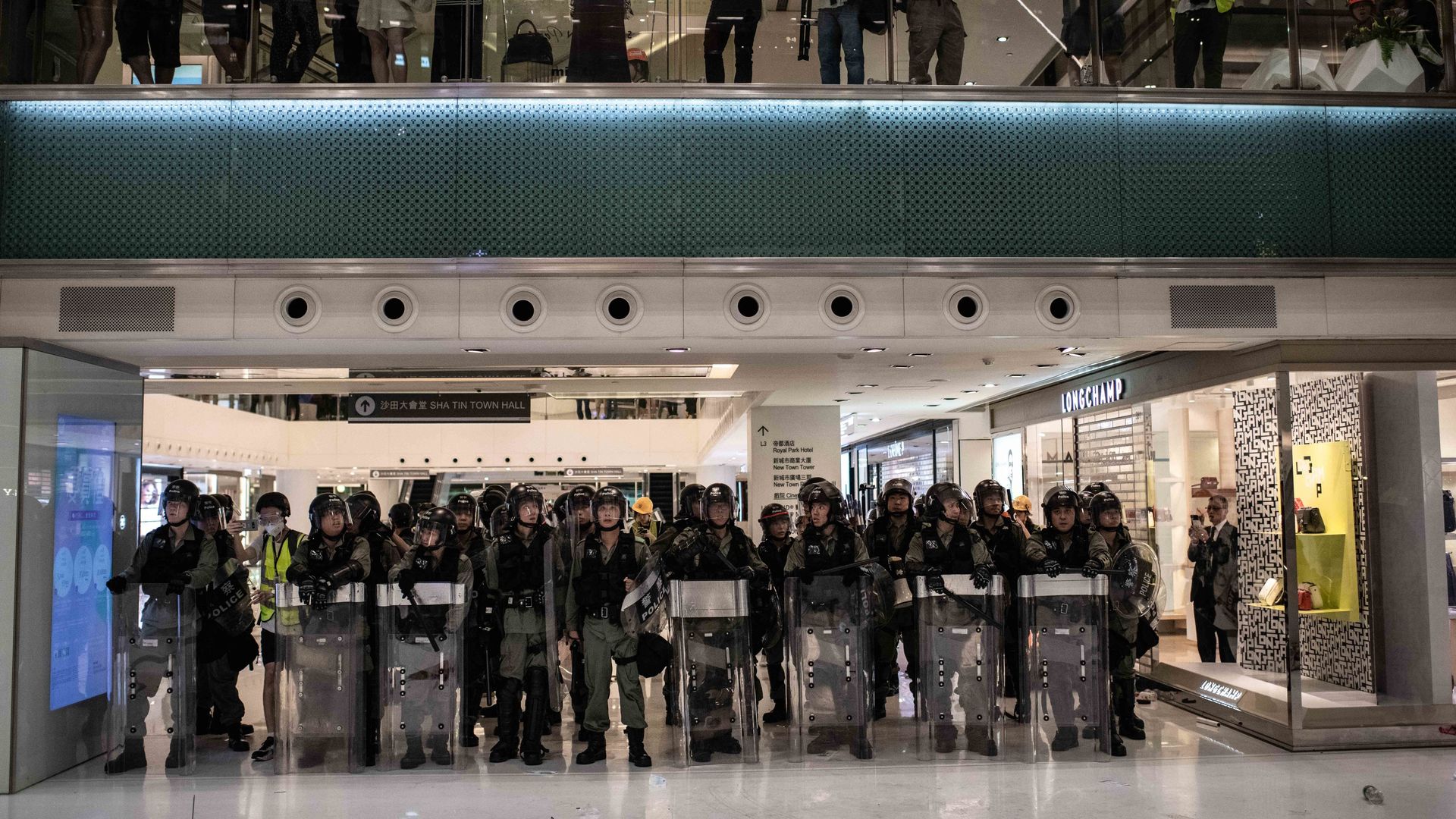 In this image, a line of riot police stand in a strip mall