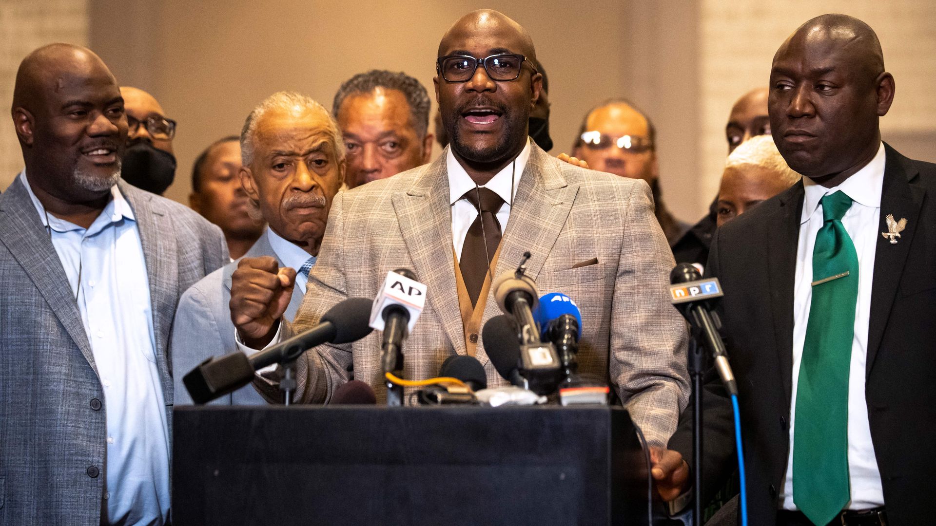 George Floyd's brother speaks into microphones at a podium, standing next to Attorney Ben Crump 