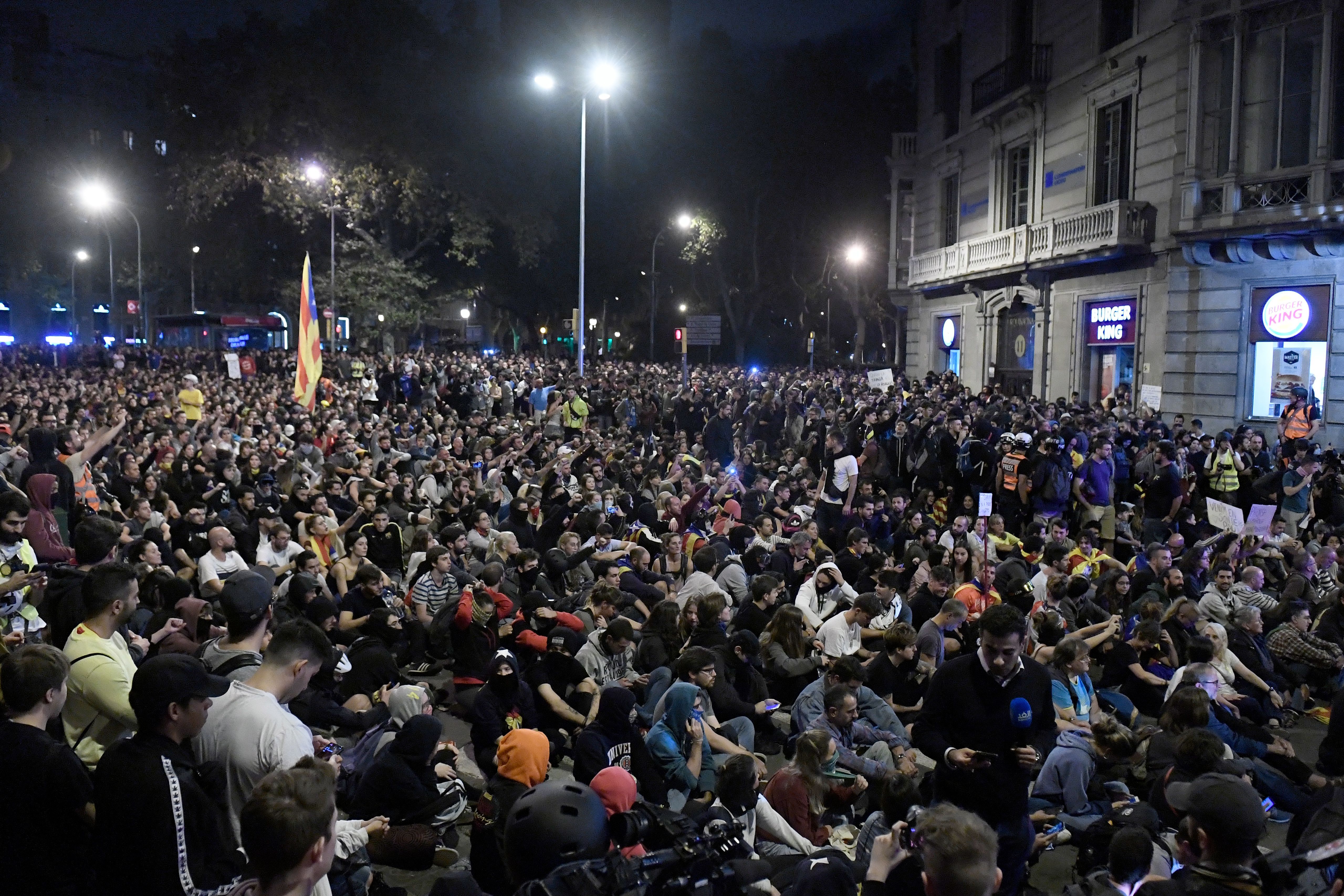 In this image, a huge crowd of people sits in a square at night