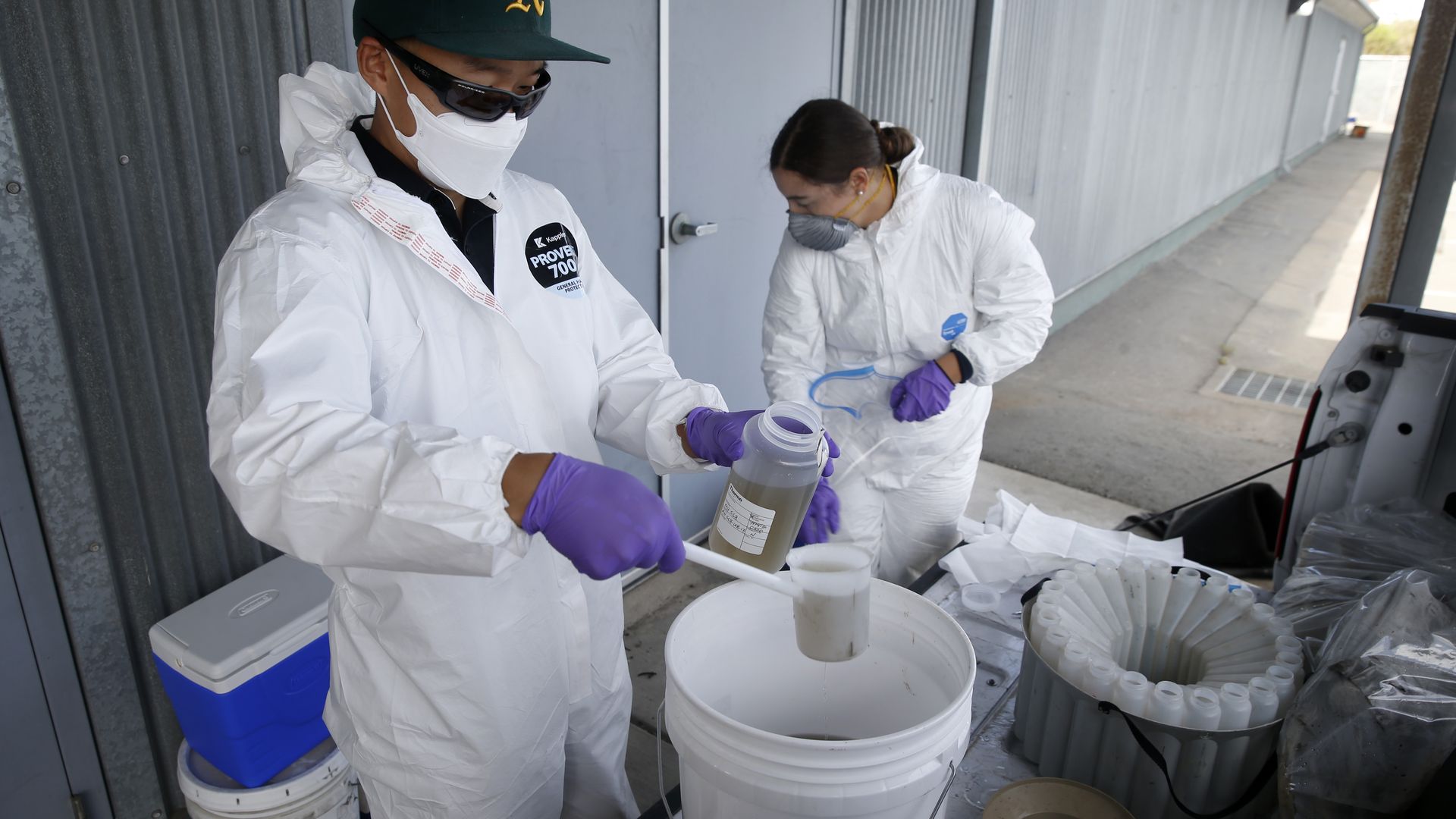 Photo of two workers in hazmat suits handling samples of wastewater